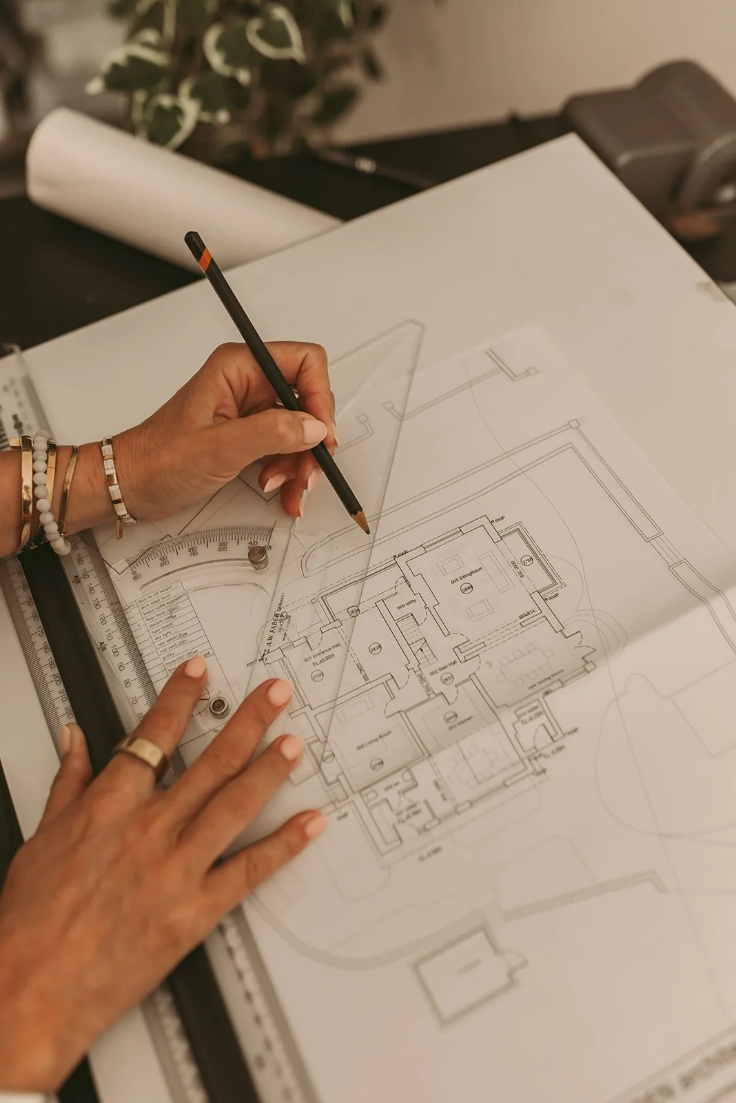 Hands working on architectural blueprints, using a ruler and compass on a drafting table.