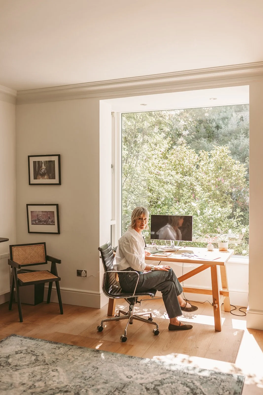 Lorraine Abel, Interior Designer Wicklow sitting at a desk in a bright room with large window and green trees outside.