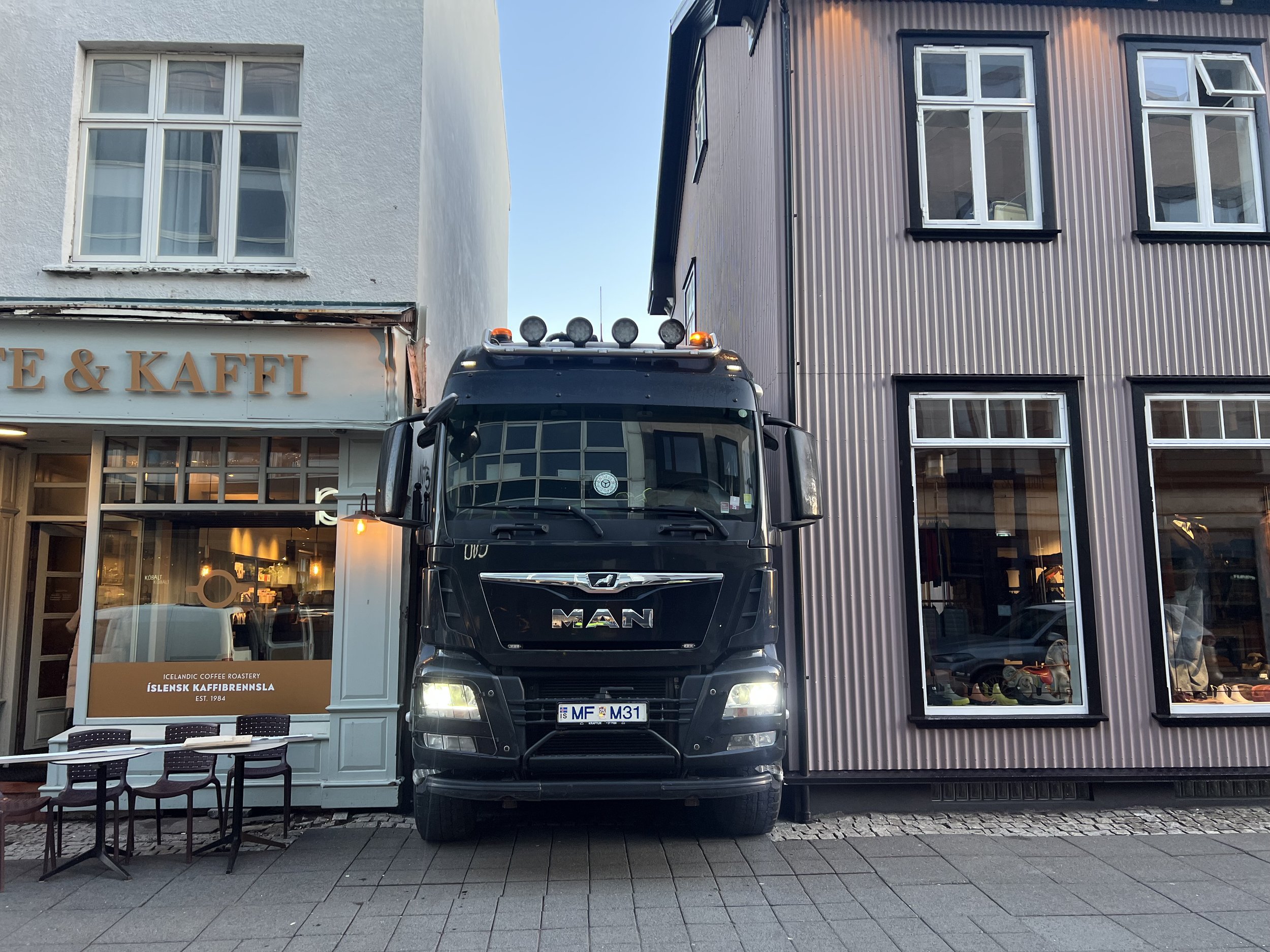 Black MAN truck parked in front of Icelandic coffee roastery with outdoor seating and neighboring buildings.