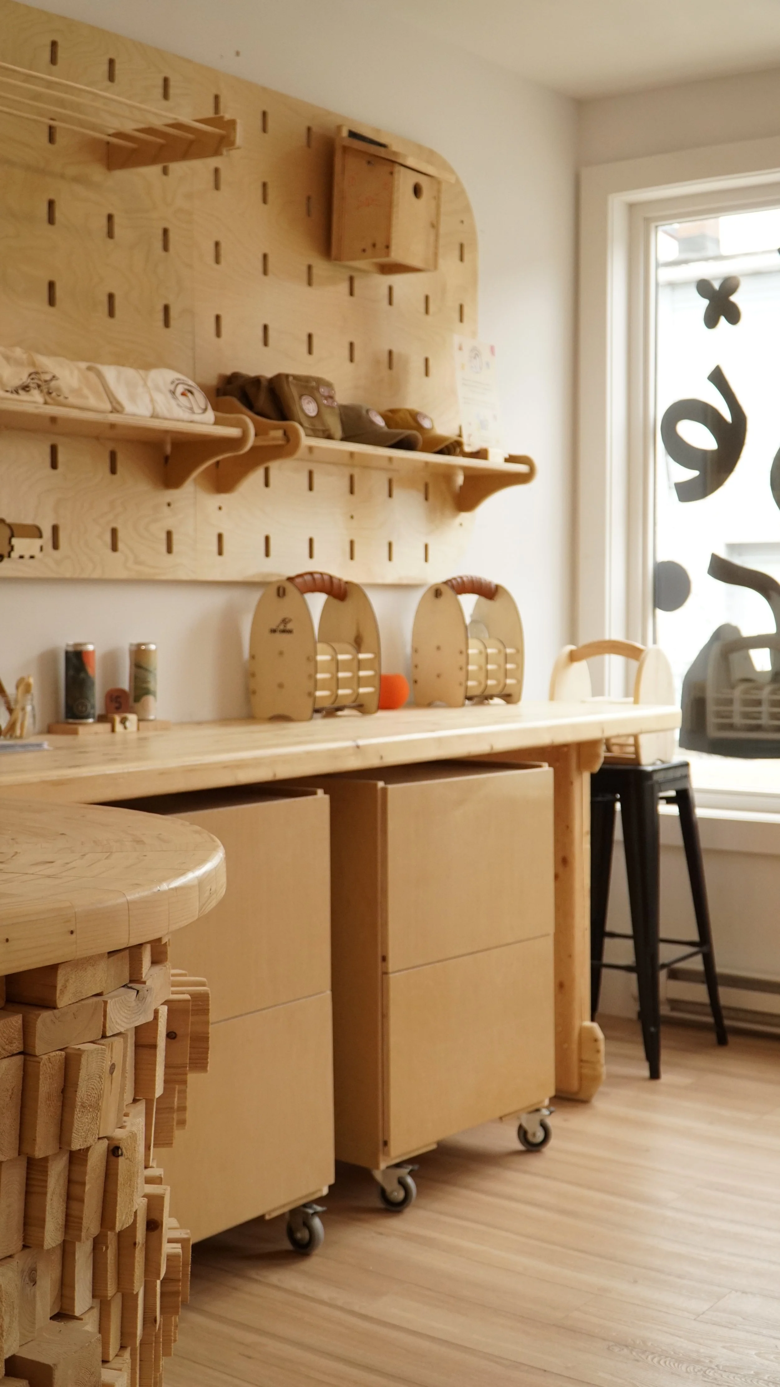 A woodworking or craft workshop with wooden furniture, shelves, and storage units, near a window with decorative stickers.