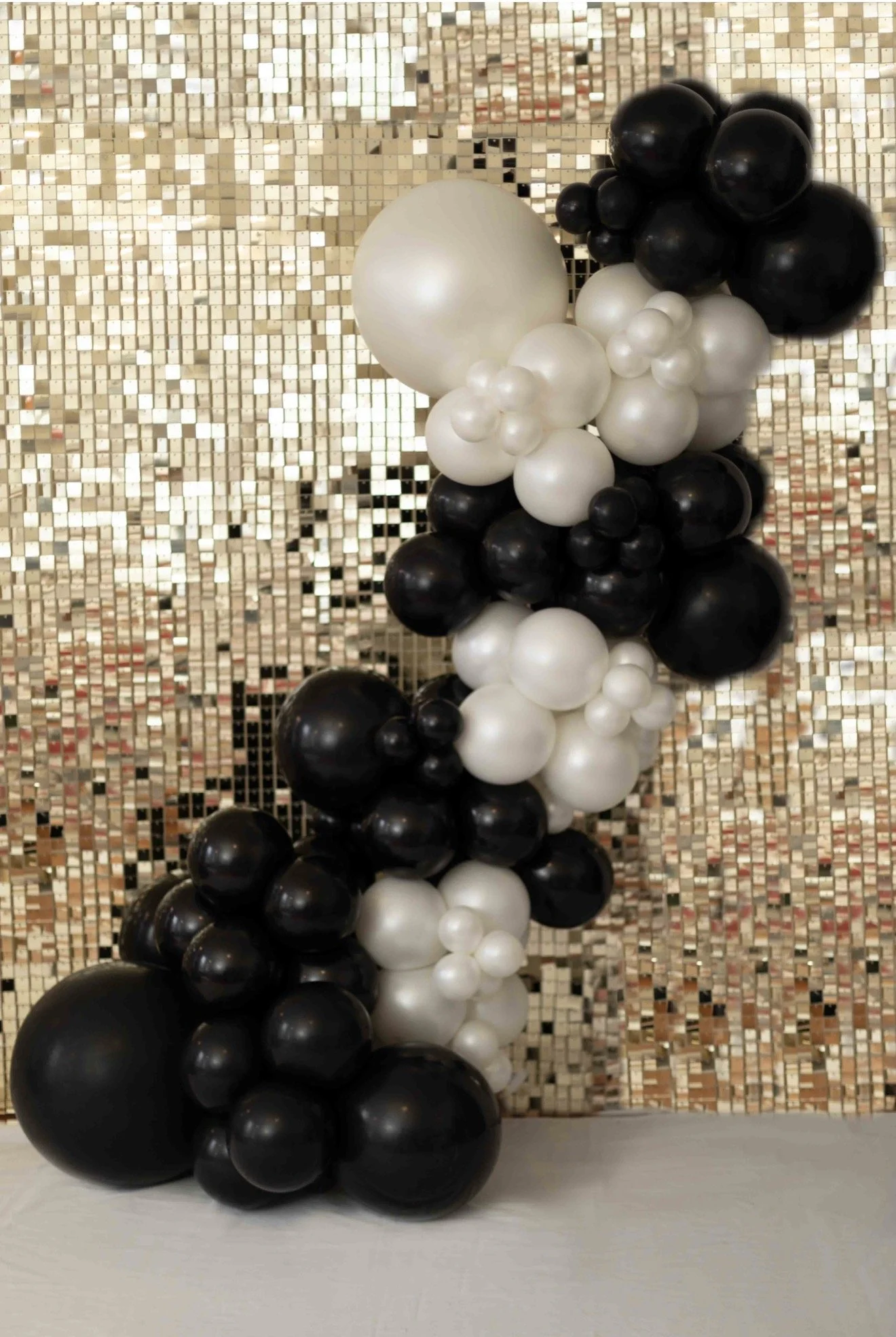 Black and pearl color balloon garland and gold shimmer wall.
