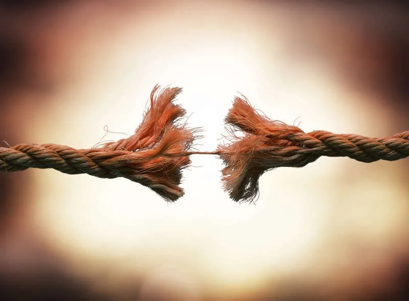 A close-up of two frayed ends of a twisted rope about to fray apart.