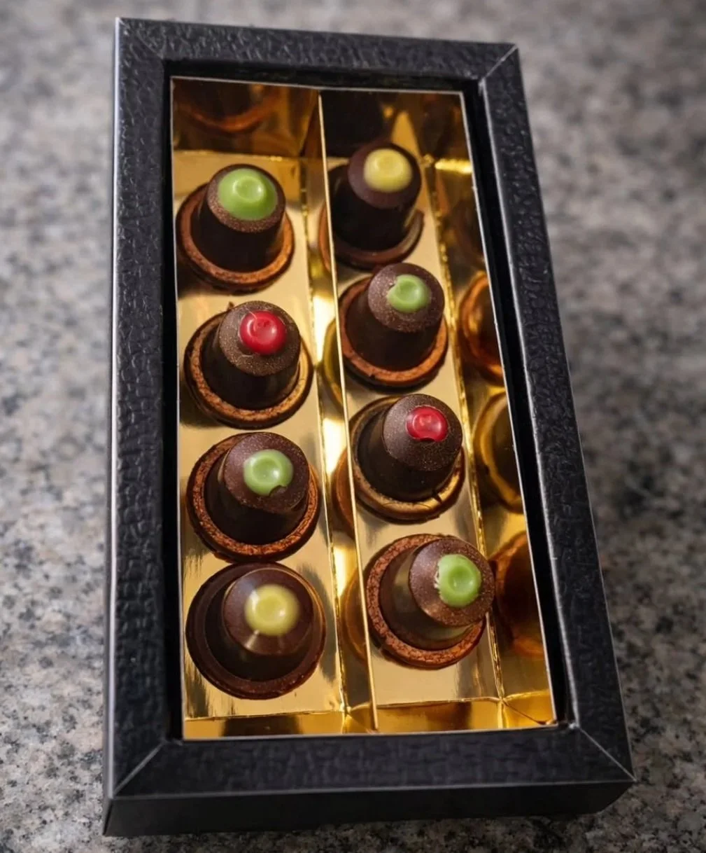 Coffret de chocolats au thé créés par Carla Campo et Charles Darzacq avec des toppings colorés, dans un emballage noir avec intérieur doré.