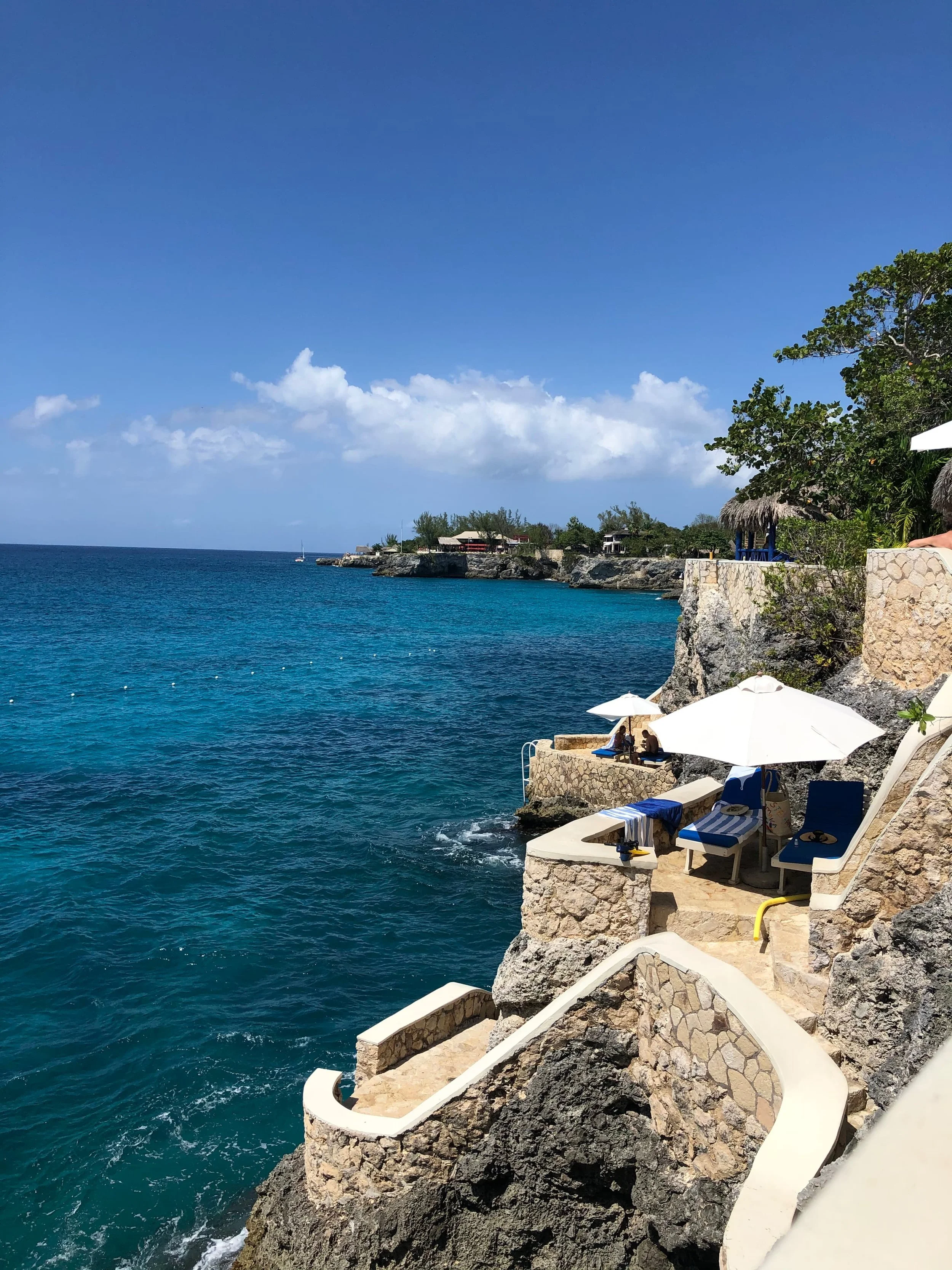 Jamaica’s The Caves in Negril — stone steps and loungers on a rocky cliff above deep turquoise water.