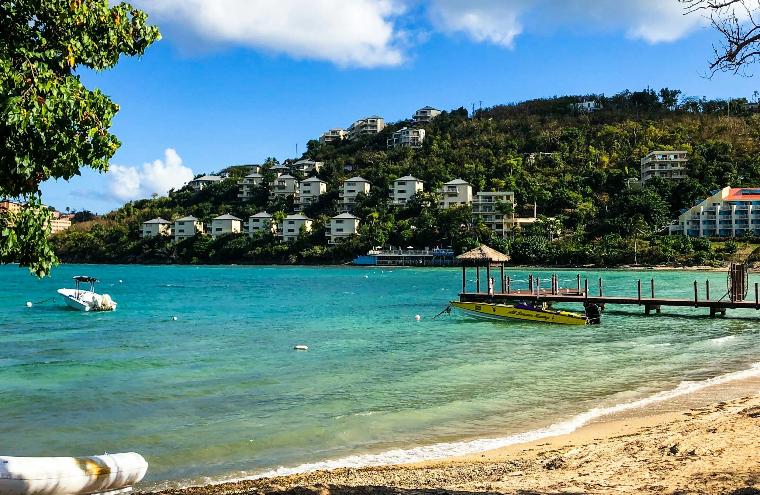 Calm turquoise bay in St. Thomas, USVI — wooden dock, moored boats, and green hillside with buildings in the background.