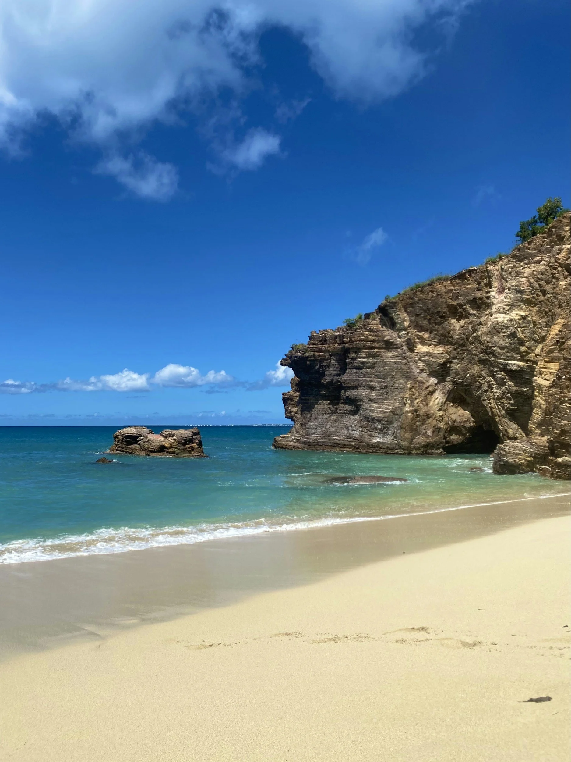 A quiet arc of golden sand meeting turquoise water beneath dramatic limestone cliffs on the French side of St. Martin