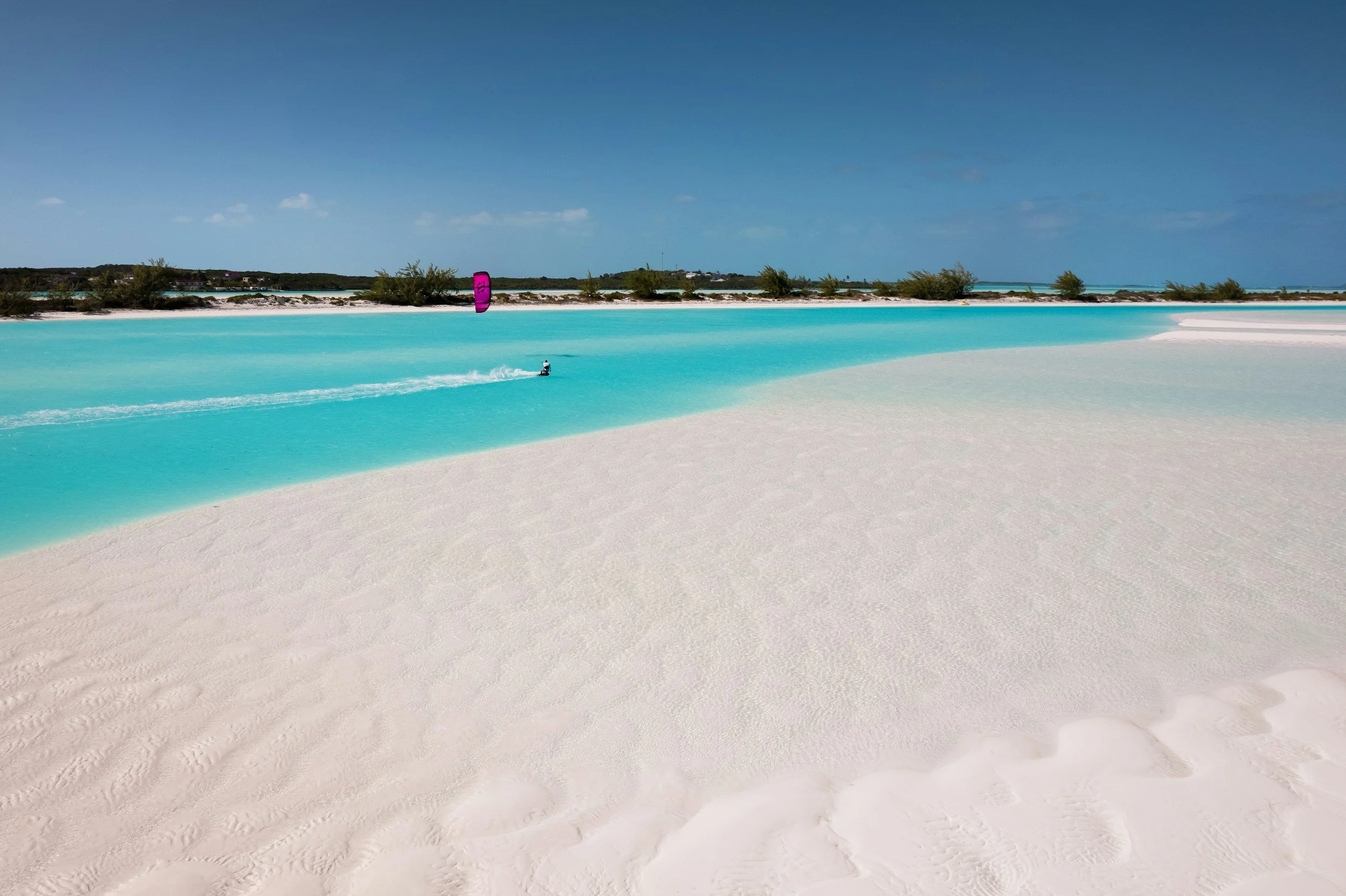White sand beach in The Exumas with calm, electric-turquoise shallows stretching to the horizon under a clear sky.