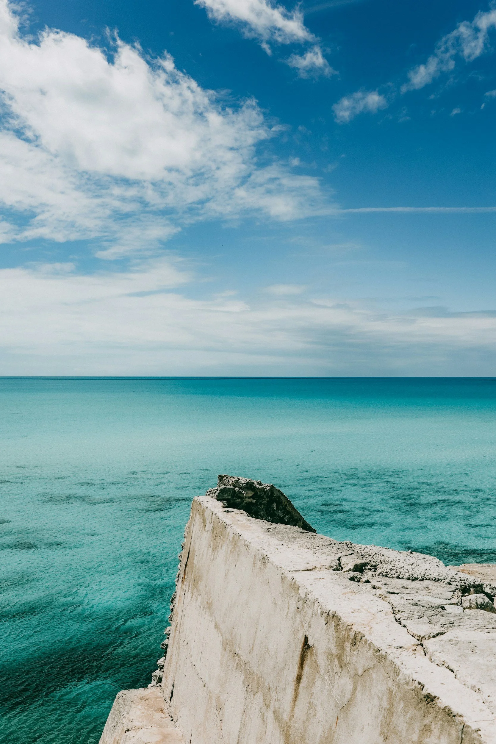 Eleuthera's narrow limestone coast where the deep Atlantic meets the shallow turquoise Bight — two oceans visible from a single point, separated by rock and road.