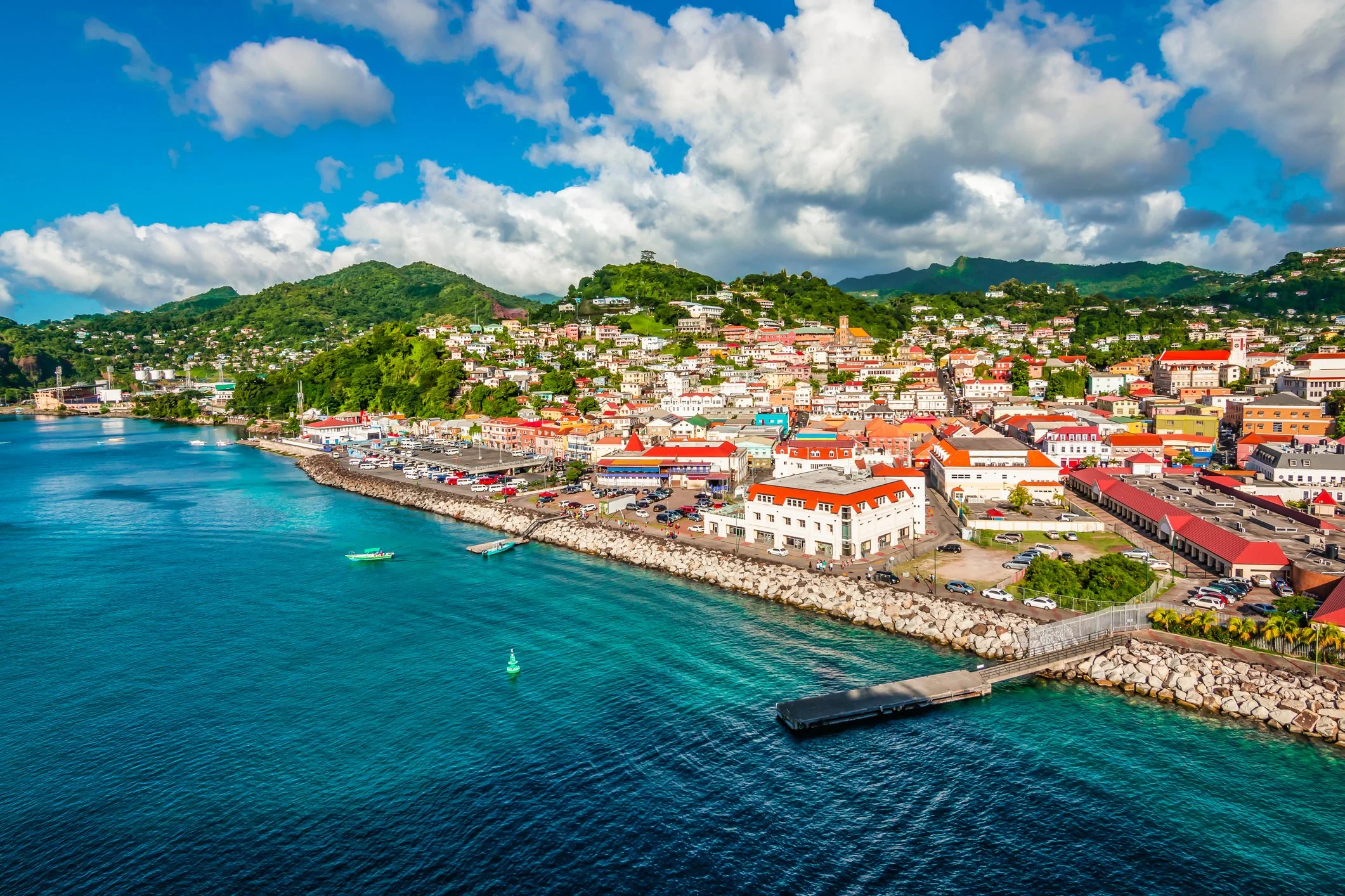 aerial view of St. George in Grenada with a boulder lined harbor and colorful buildings against a lush small mountain