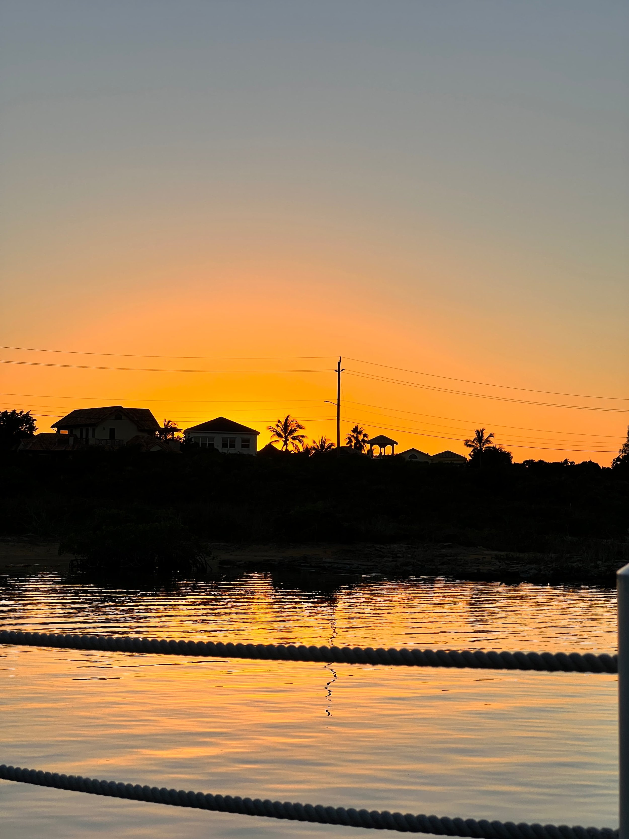 Turks and Caicos sunset over calm water with silhouetted houses and palm trees glowing orange.