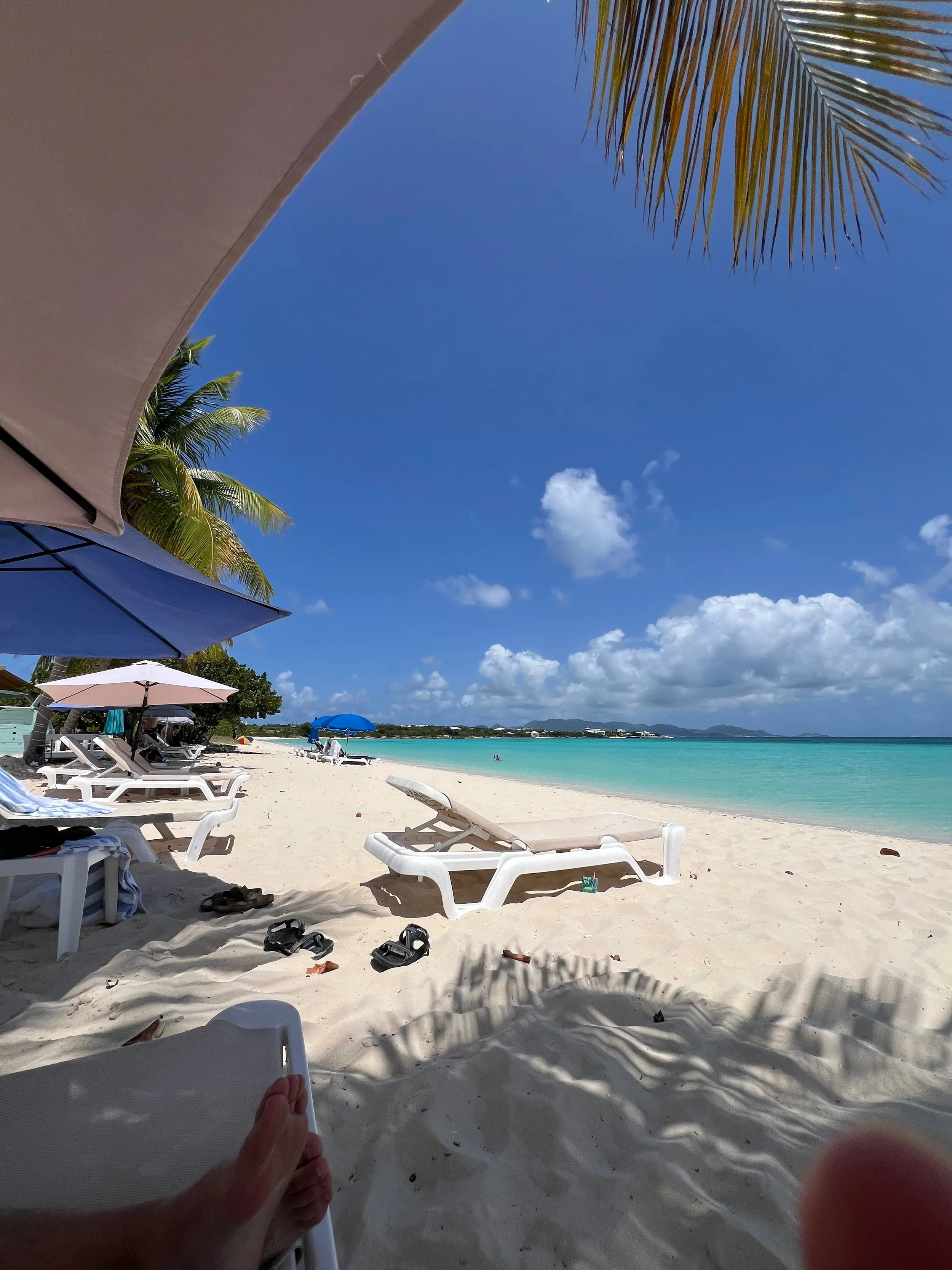 View from a shaded beach chair at Rendezvous Bay in Anguilla, with calm turquoise water and soft white sand.