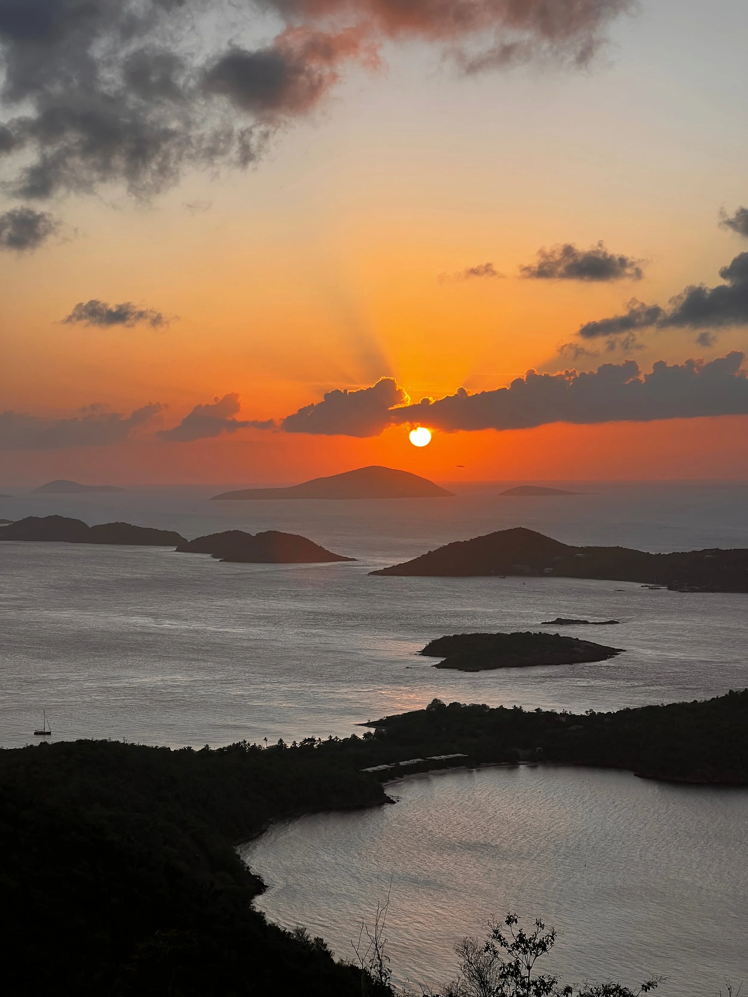 Sunset over the ocean near St. John, USVI, with low islands silhouetted on the horizon beneath orange and pink clouds.