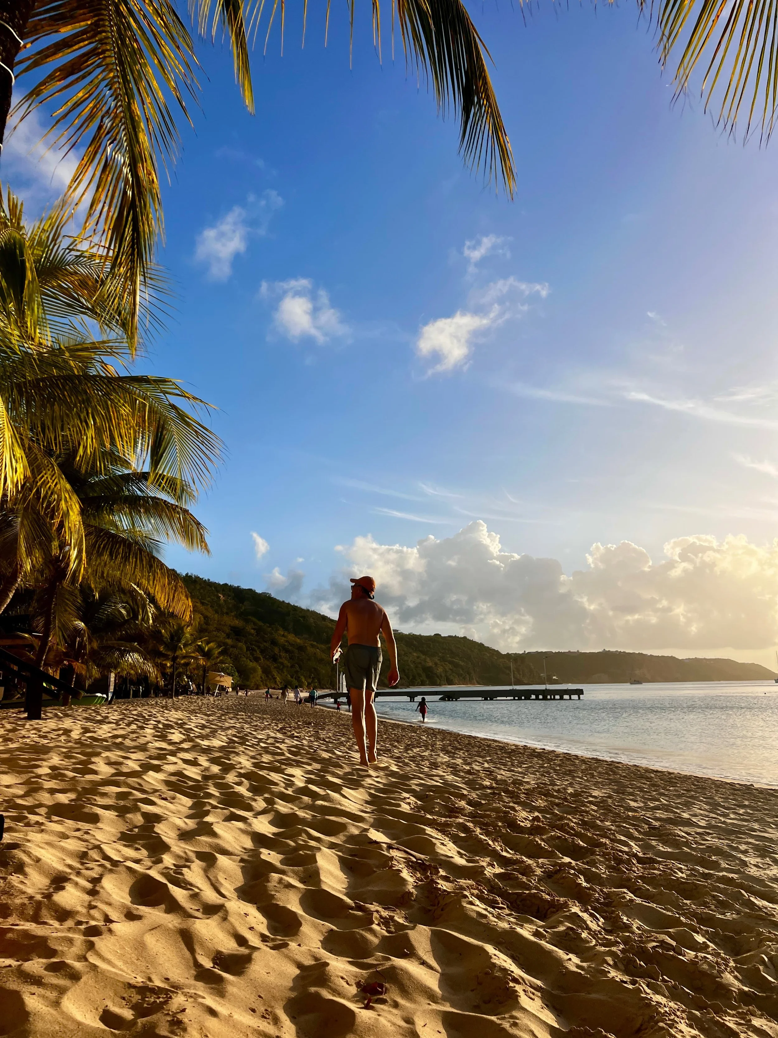 Man walking along Anguilla’s quiet beach at golden hour under palm trees and blue sky.