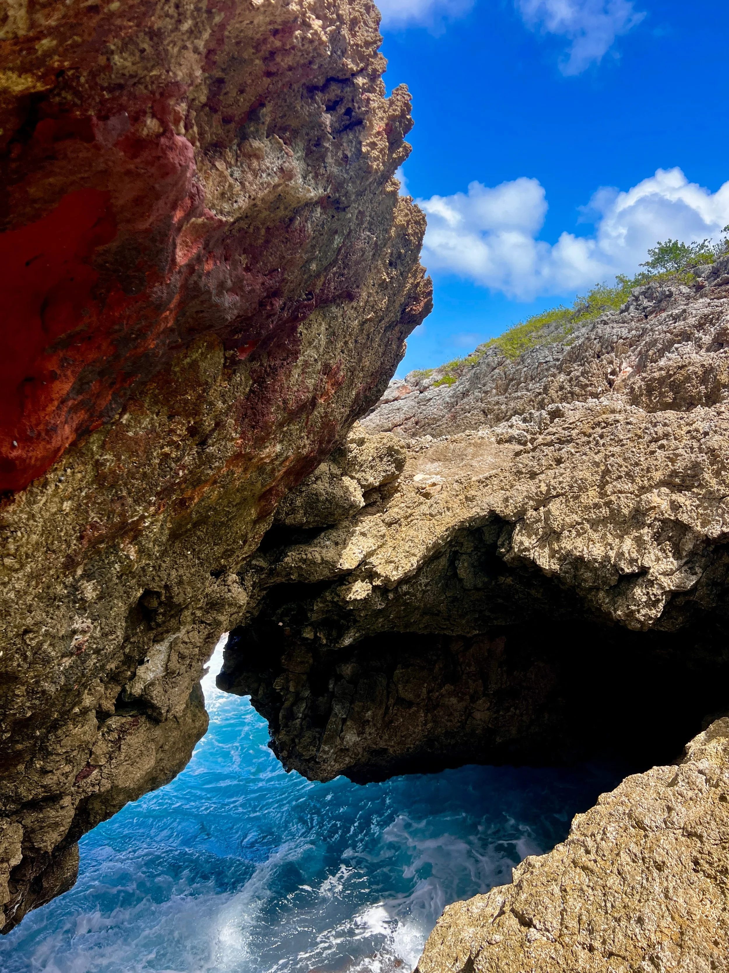 Natural sea cave on Anguilla’s rocky coast where turquoise waves crash below red limestone cliffs.