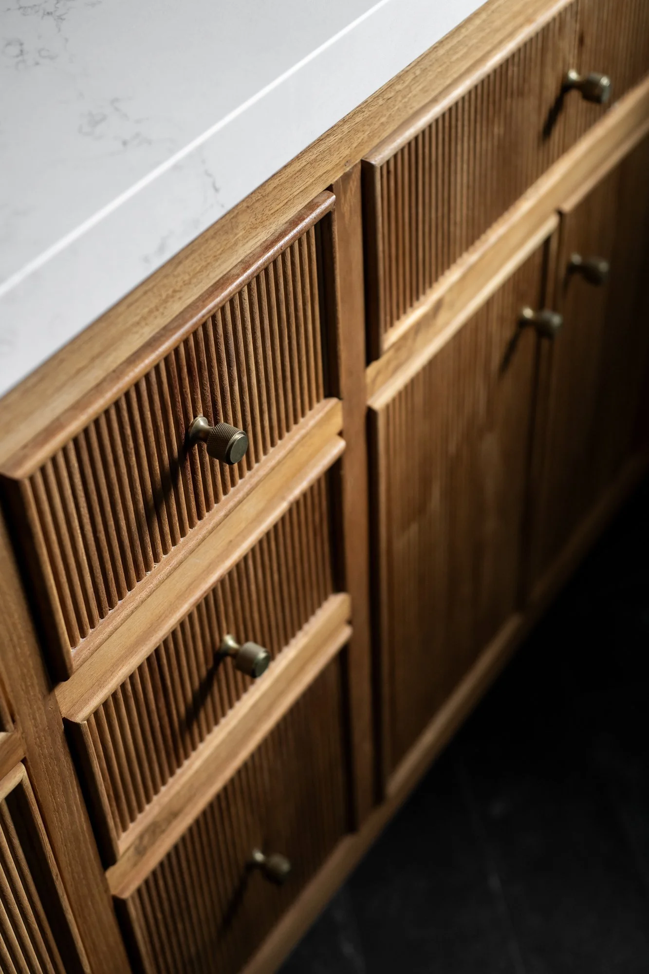 Wooden cabinet with slatted doors and small round knobs, partially visible against a white marble wall.