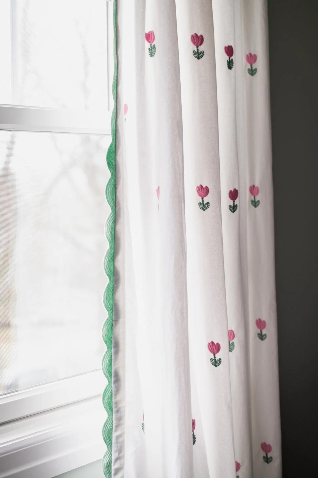 Close-up of white curtains with pink flower embroidery hanging by a window with out-of-focus background.