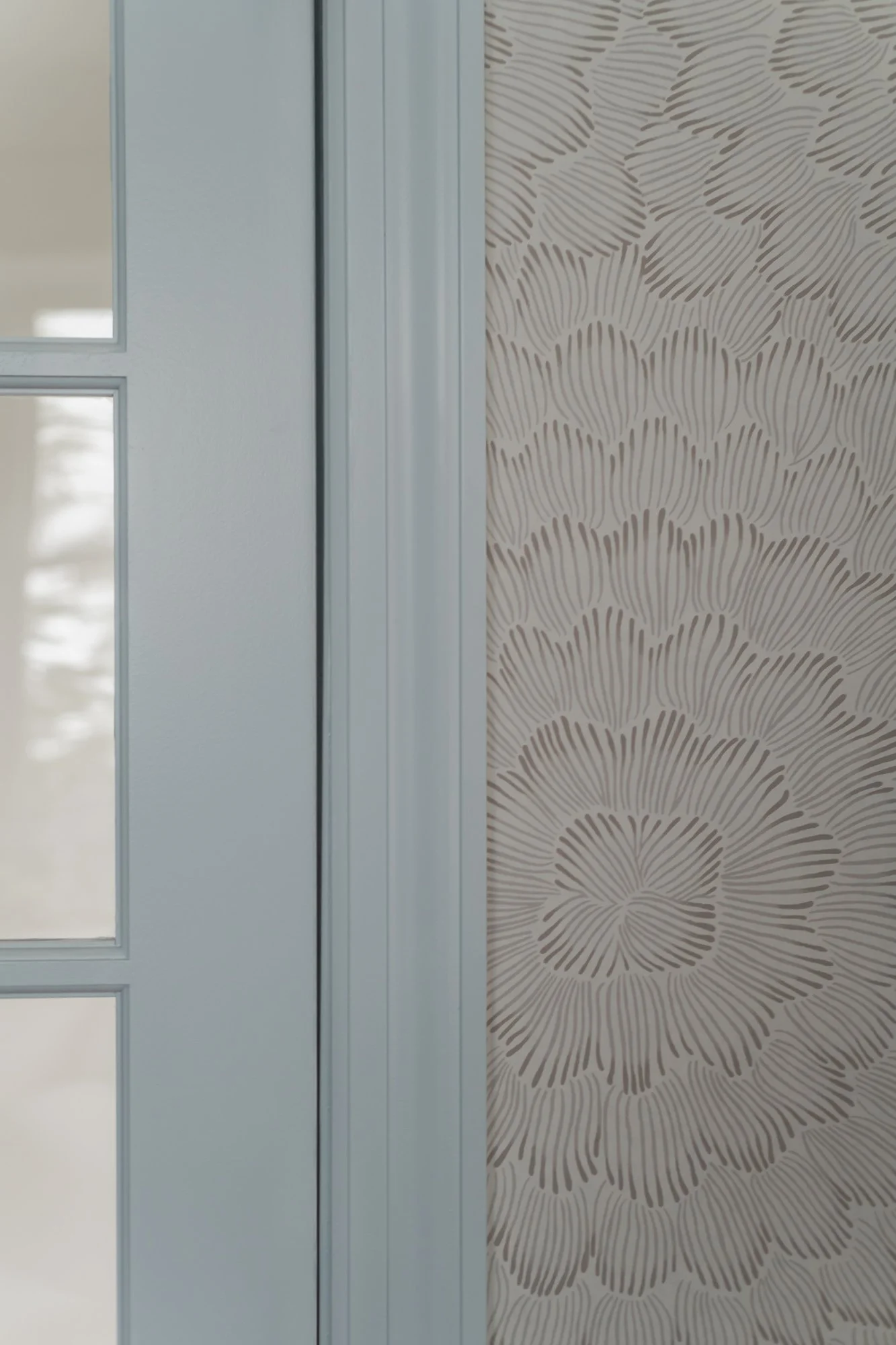 Close-up of a door with glass panels next to a wall with patterned wallpaper featuring floral designs.