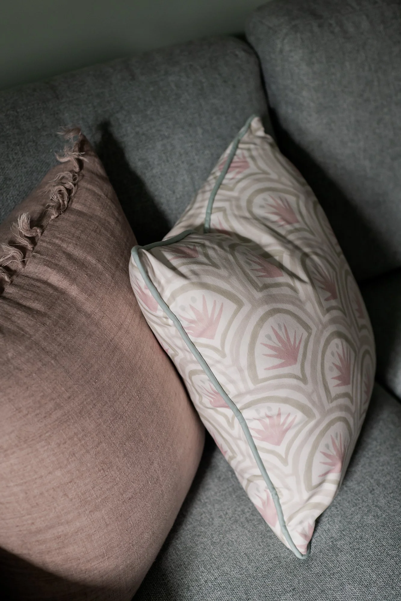 Close-up of two throw pillows on a gray fabric sofa, one brown with fringe trim and the other with a pastel geometric pattern.