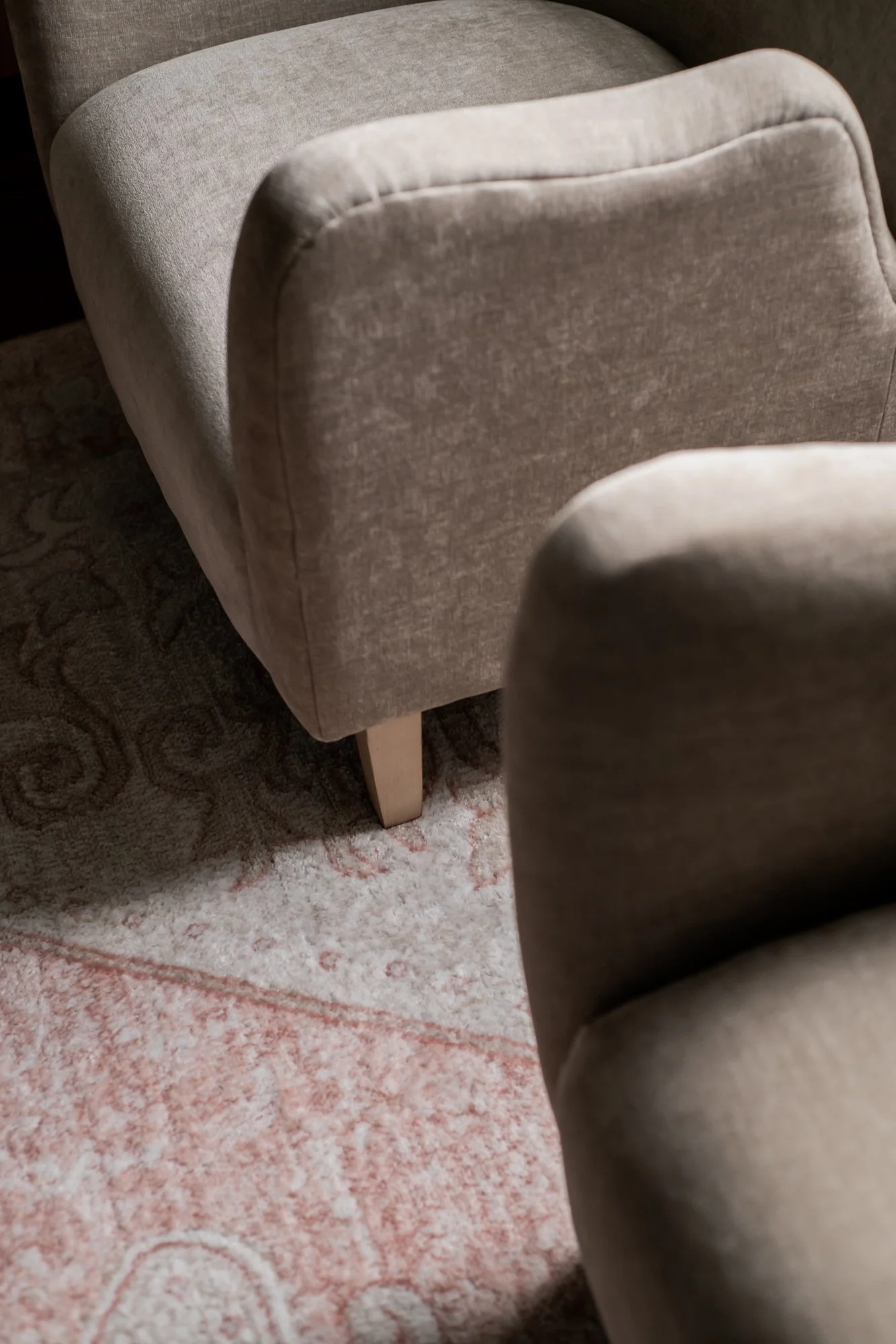 Close-up of two beige upholstered armchairs on a patterned area rug.