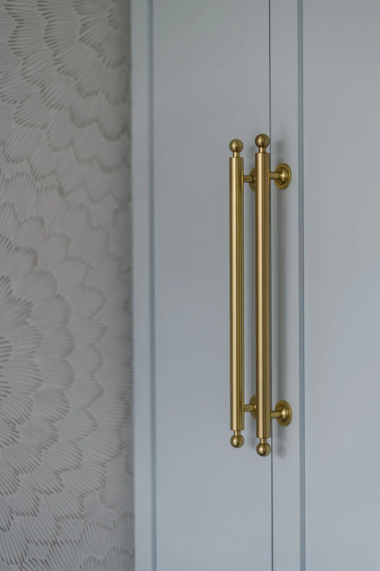 Close-up of gold-colored door handles on a light gray door, with patterned wallpaper on the left side.