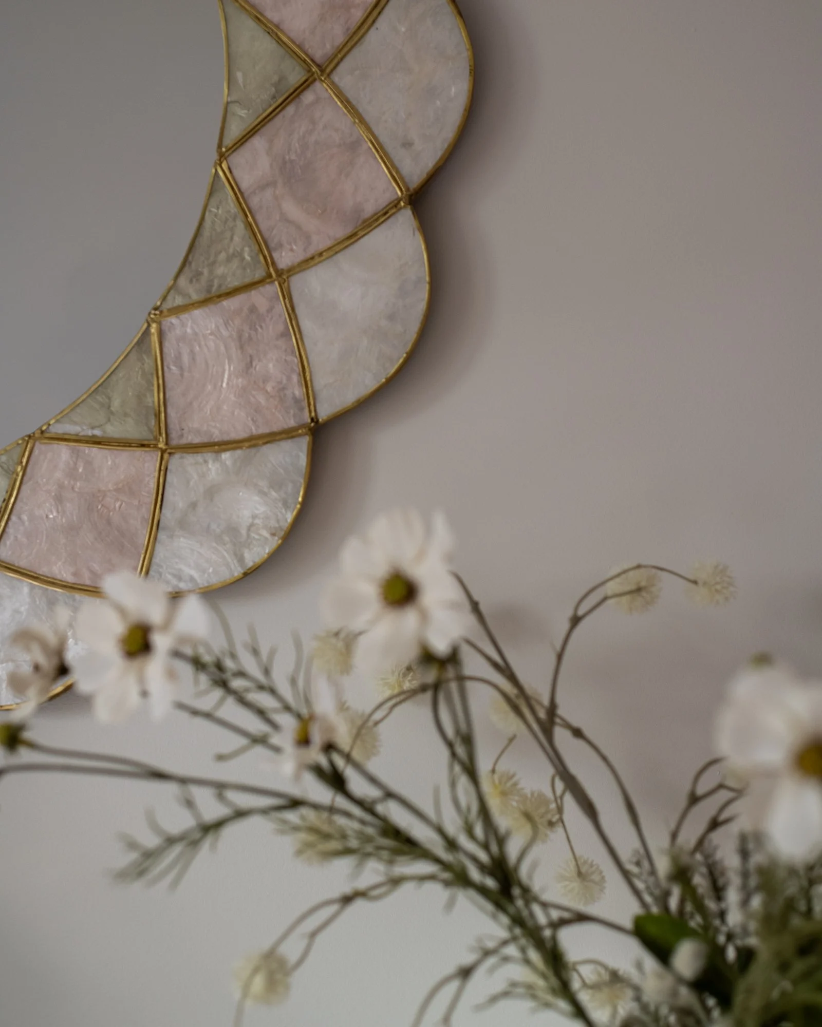Decorative wall art with a gold frame and pastel-colored shell pieces, and a bouquet of white and cream flowers in the foreground.