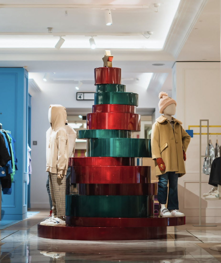 Display of child's mannequins and a colorful stepped structure in a clothing store, with mannequins dressed in winter clothing.
