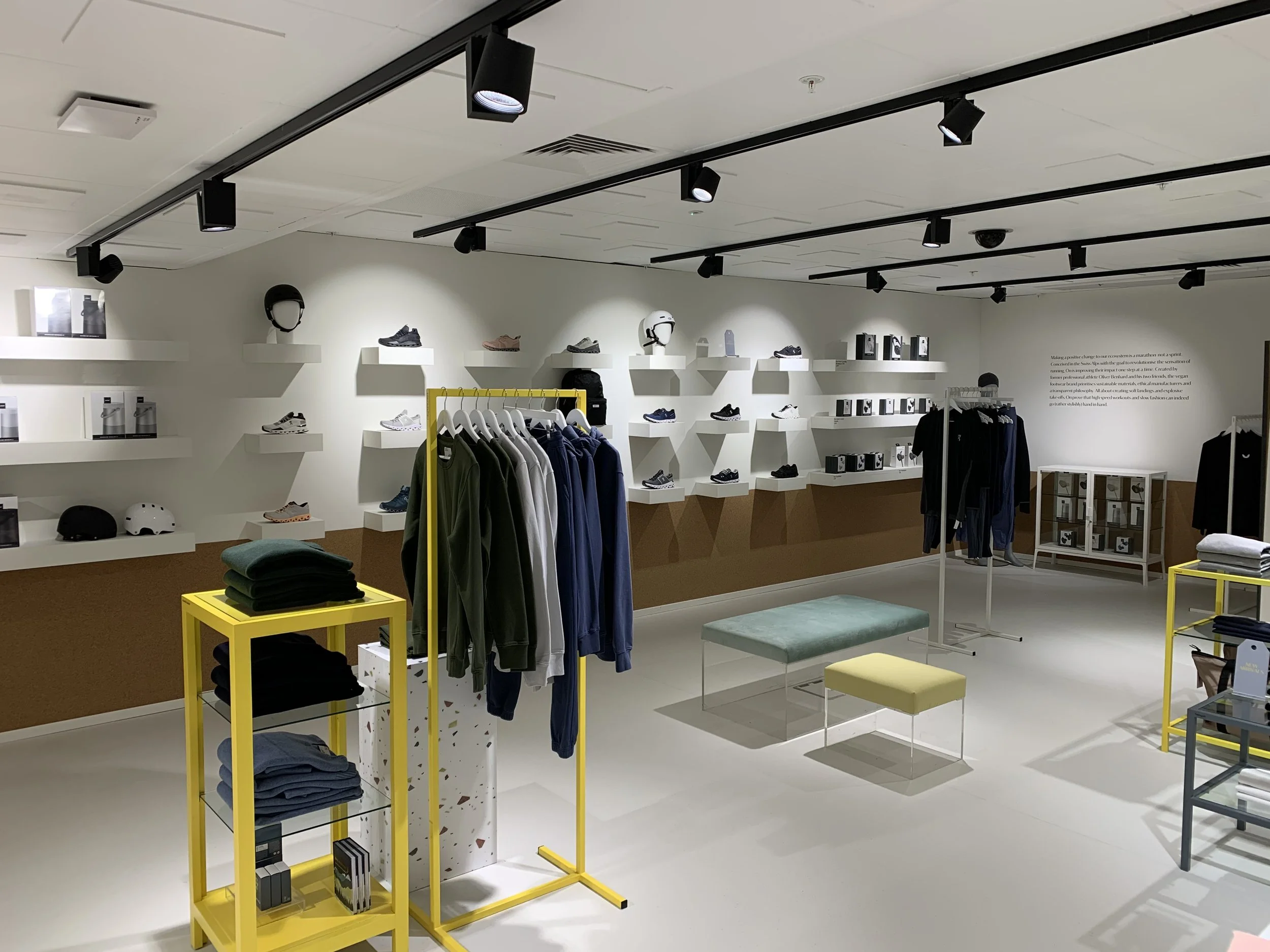 Interior of a retail store displaying athletic shoes, helmets, apparel, and accessories with clothing racks, shelves, and seating arrangements.