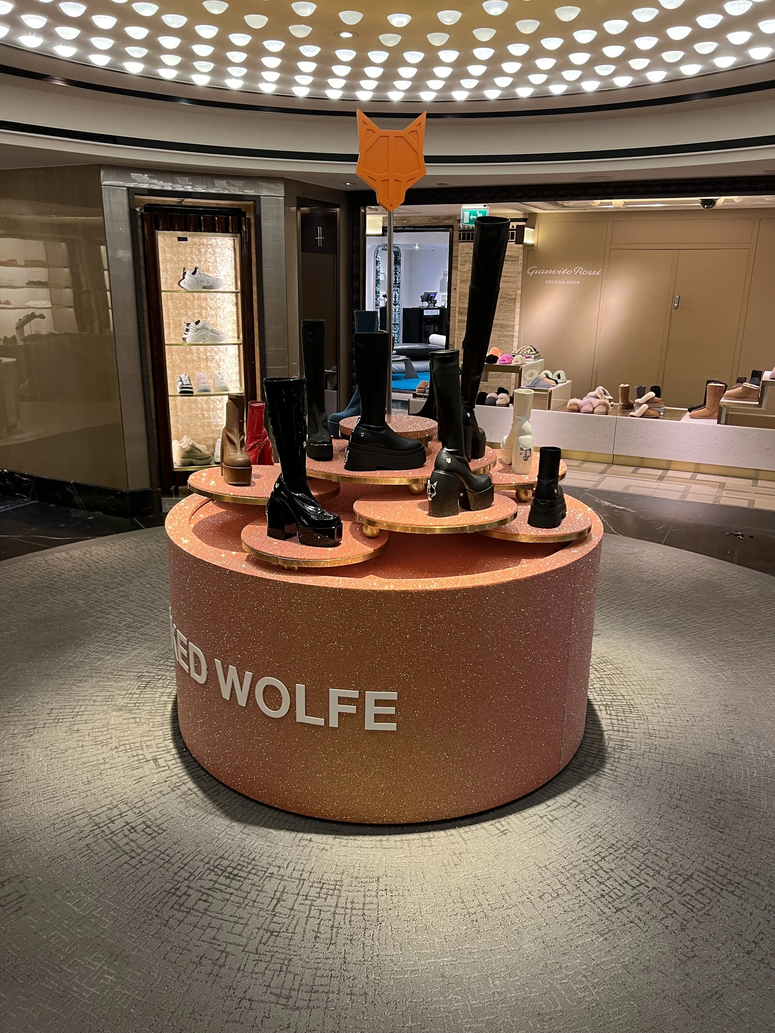 Display table with various black and brown knee-high boots and shoes in a shoe store interior.