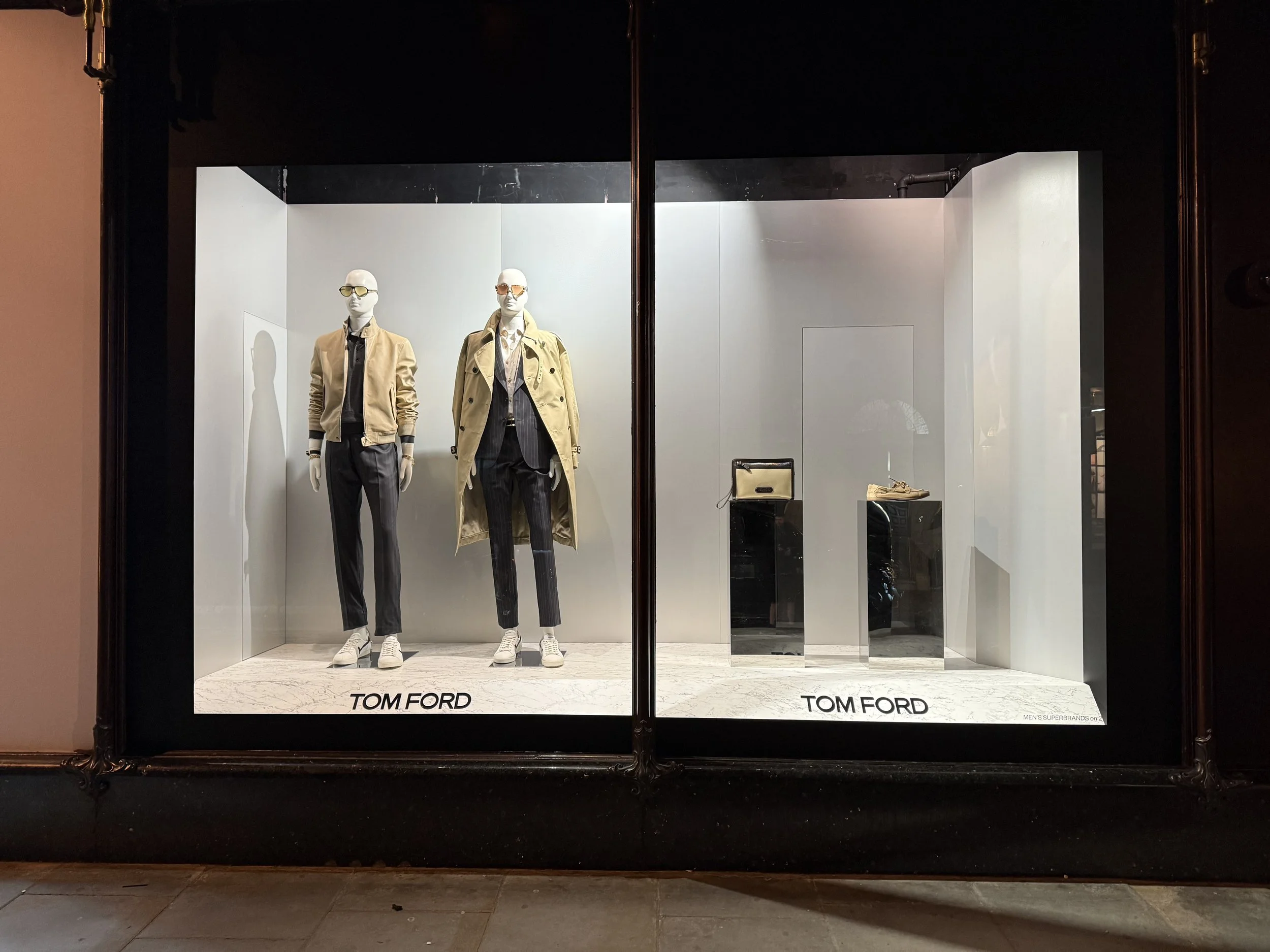 Tom Ford clothing store window display featuring two mannequins dressed in casual and business attire, with accessories on display.