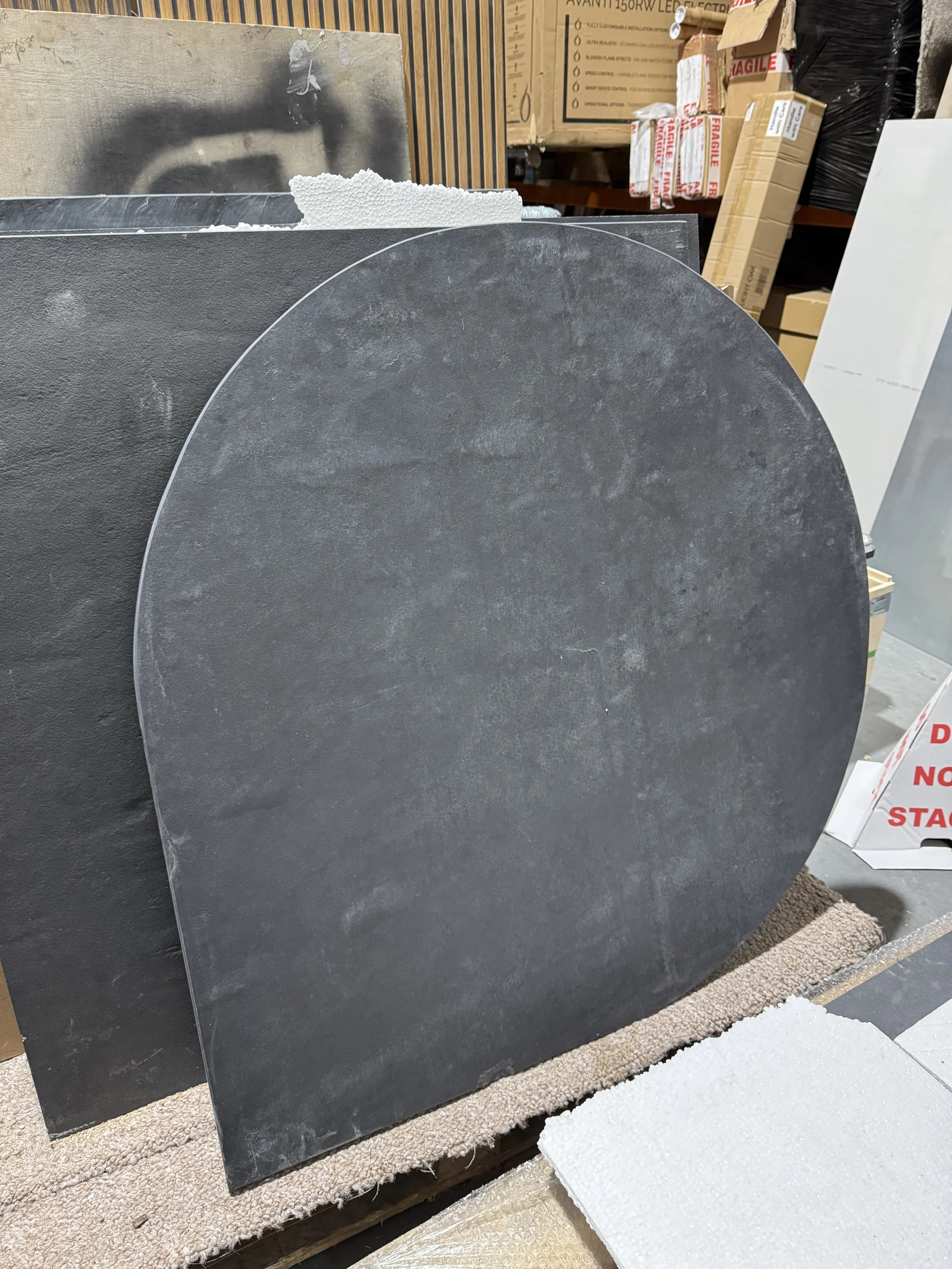 Round black stone tile leaning against a larger black rectangular tile in a warehouse setting.