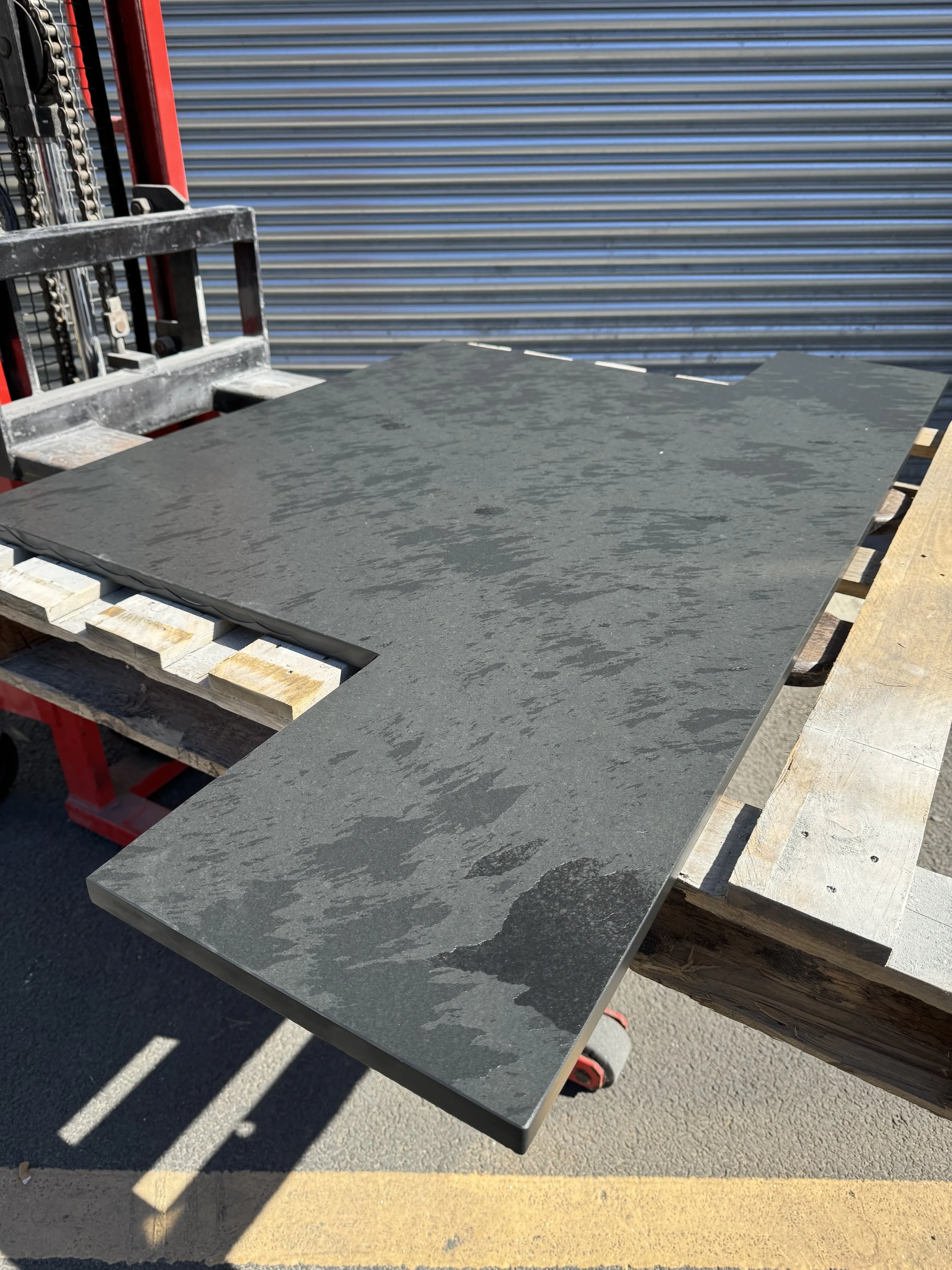 Large gray slate tile on wooden workbench outdoors with a metal shutter in the background.