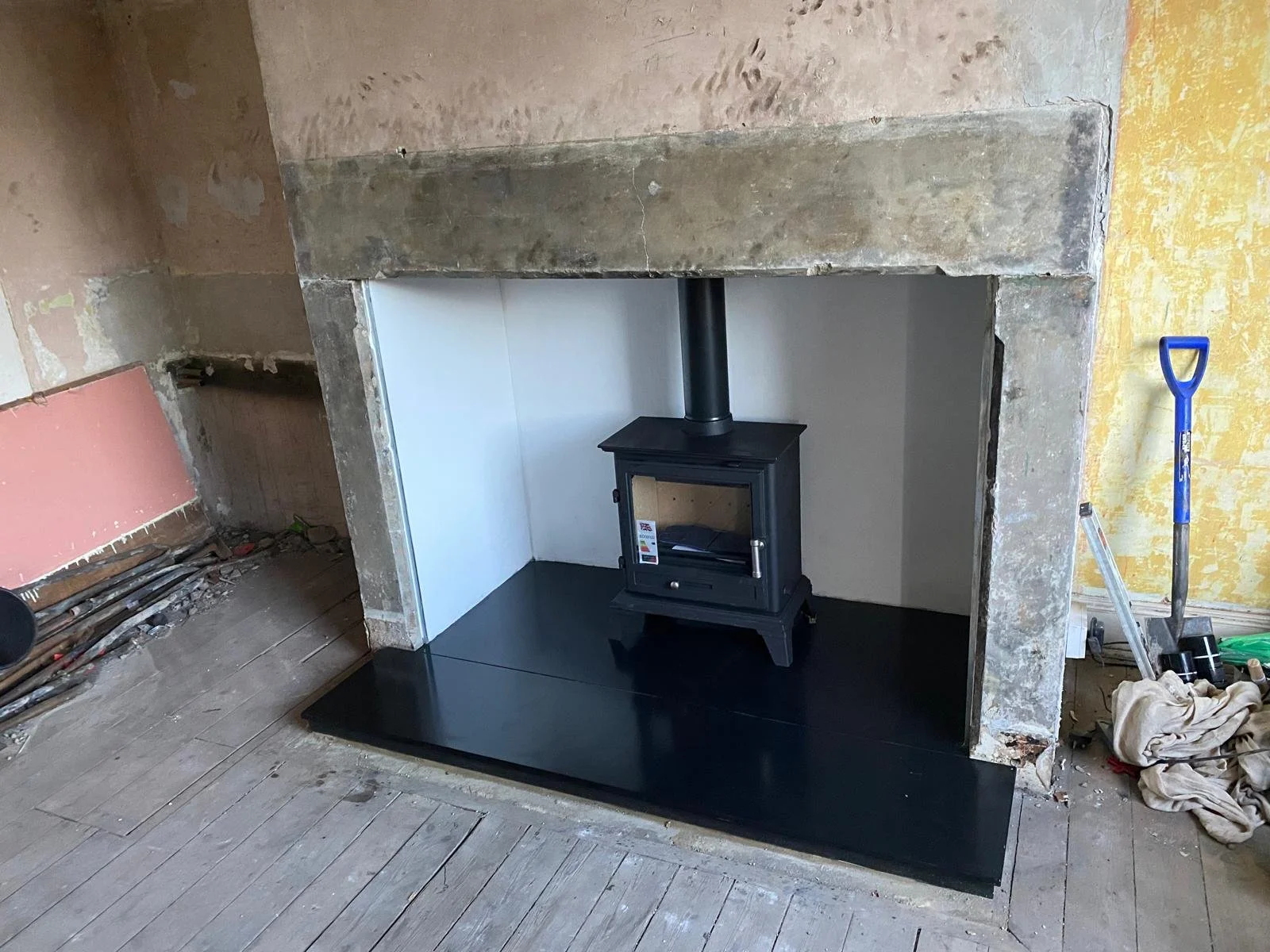 Wood-burning stove installed in a partially renovated room with surrounding wall and floor construction materials.