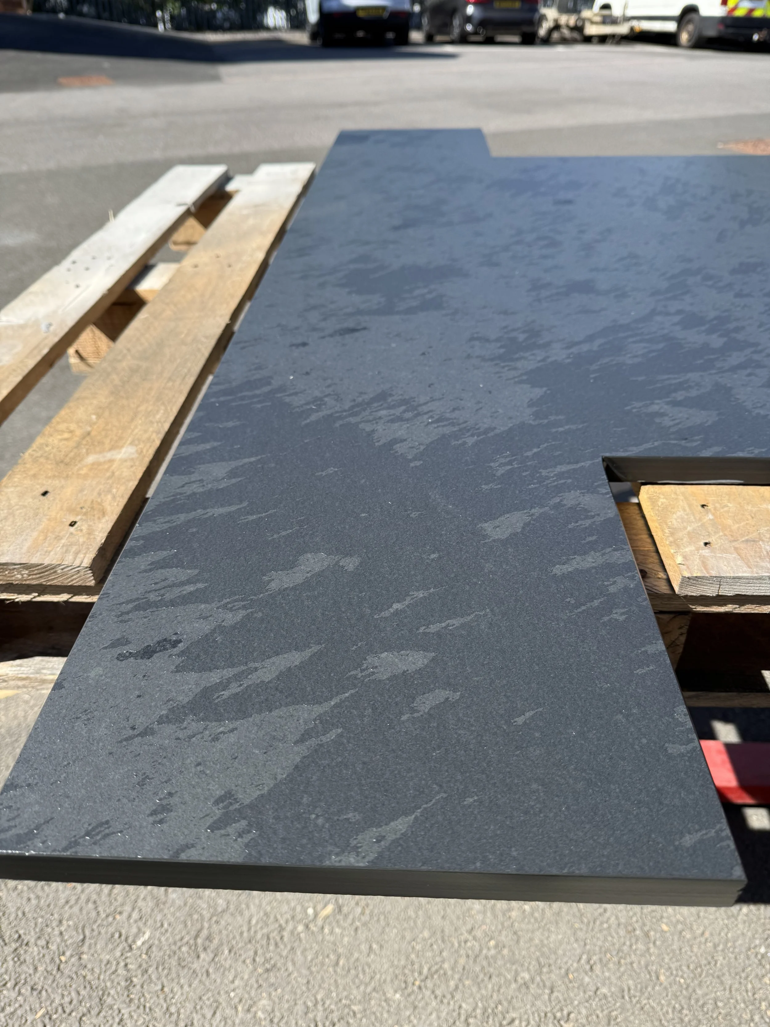 A black granite or quartz countertop with a textured surface, placed on a wooden and metal stand outdoors on a sunny day.