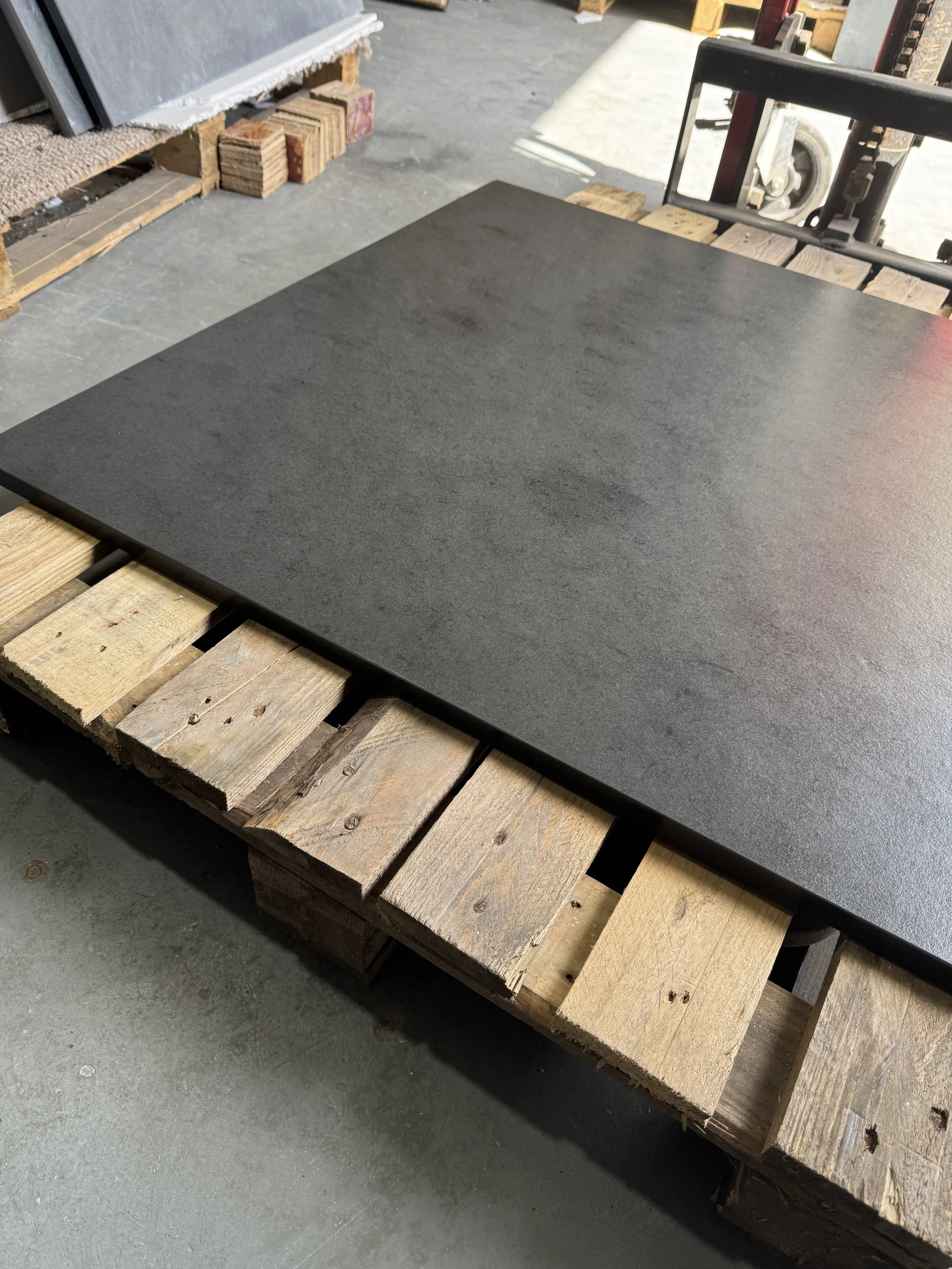 A large square black stone tile on a wooden pallet in a workshop.