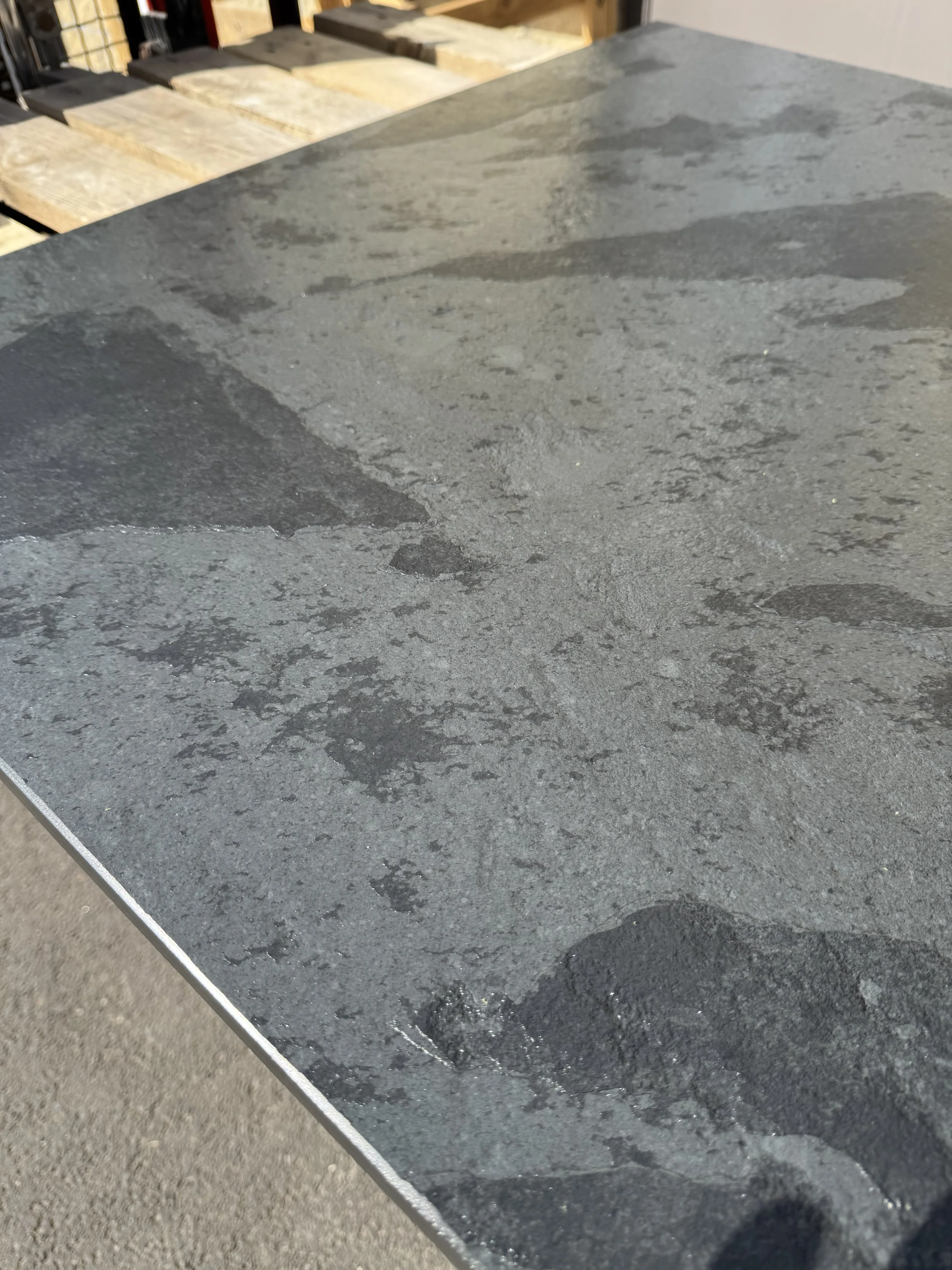 Close-up view of a dark gray, textured stone or slate countertop with water stains and a rough surface.