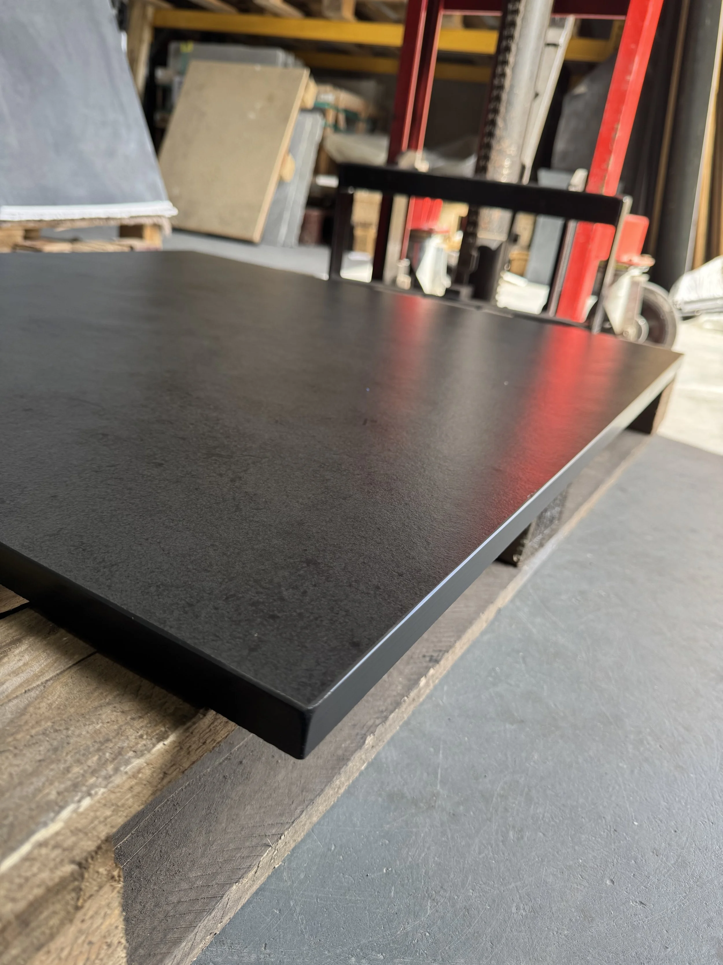 A black countertop in a workshop or warehouse setting, with some tools and materials in the background.