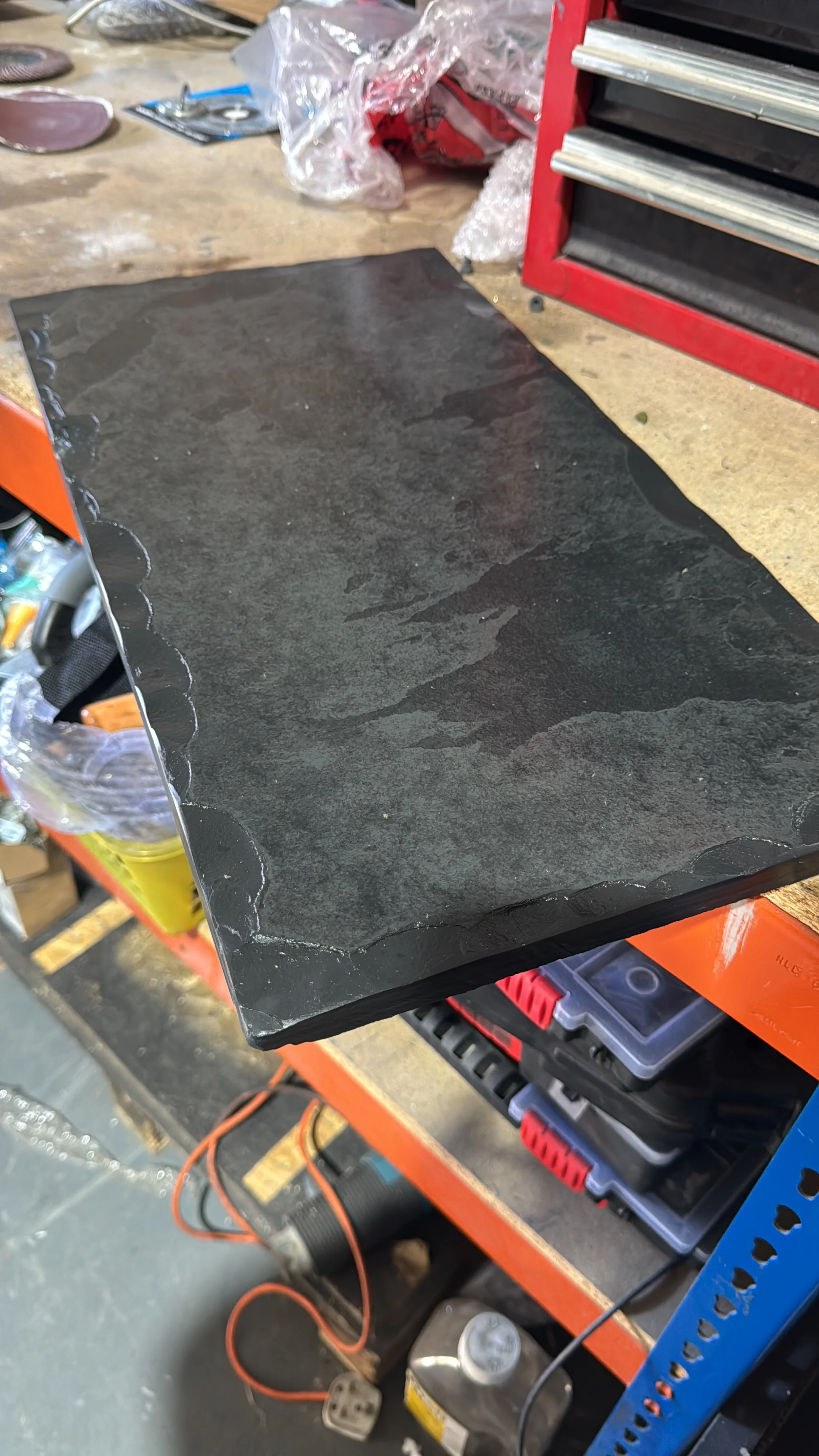 Black slate tile with uneven, scalloped edges on a workbench in a workshop.