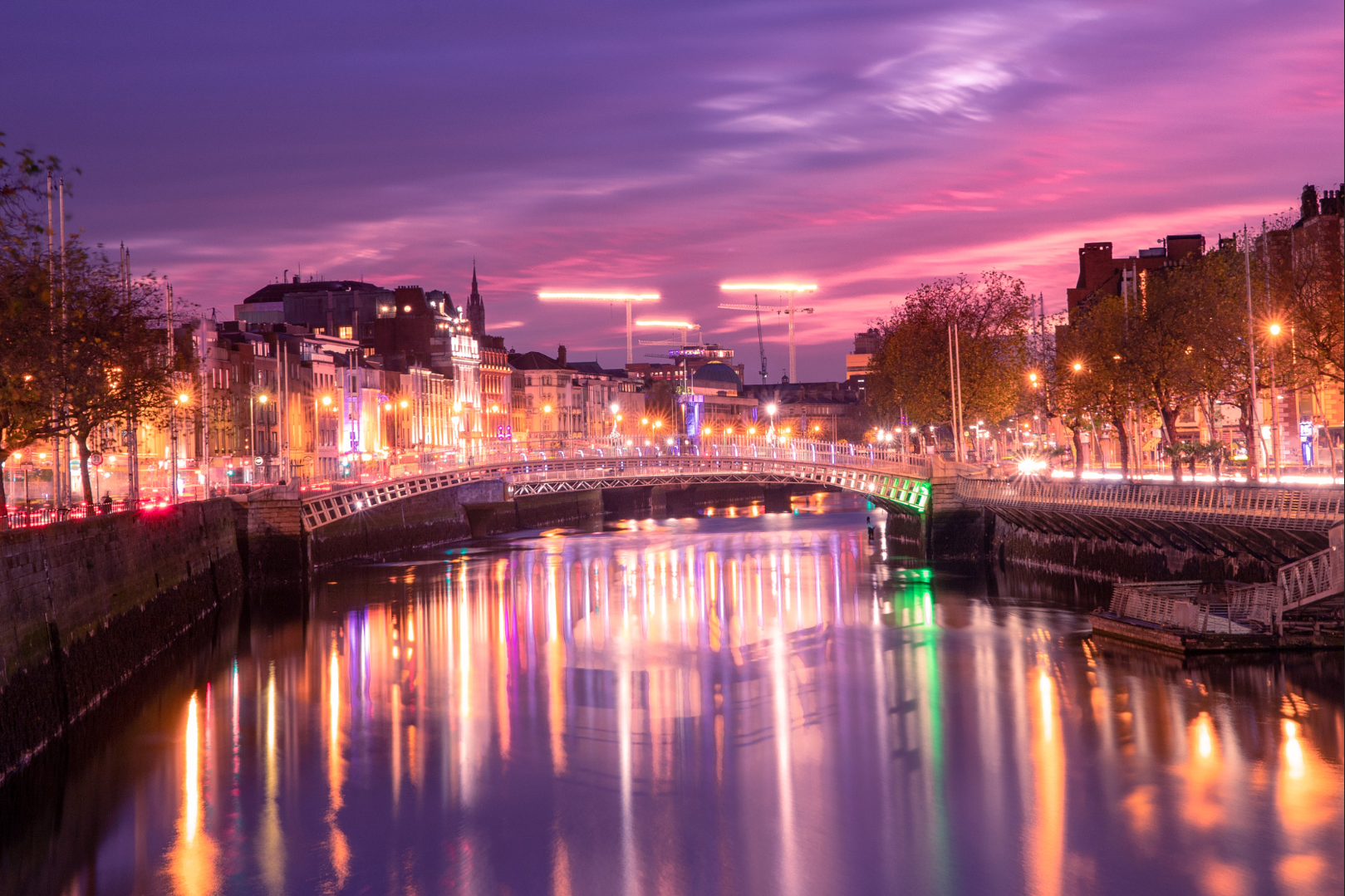 Sunset over the River Liffey in Dublin, Ireland with the city lights reflected in the water and Ha' Penny Bridge in the distance