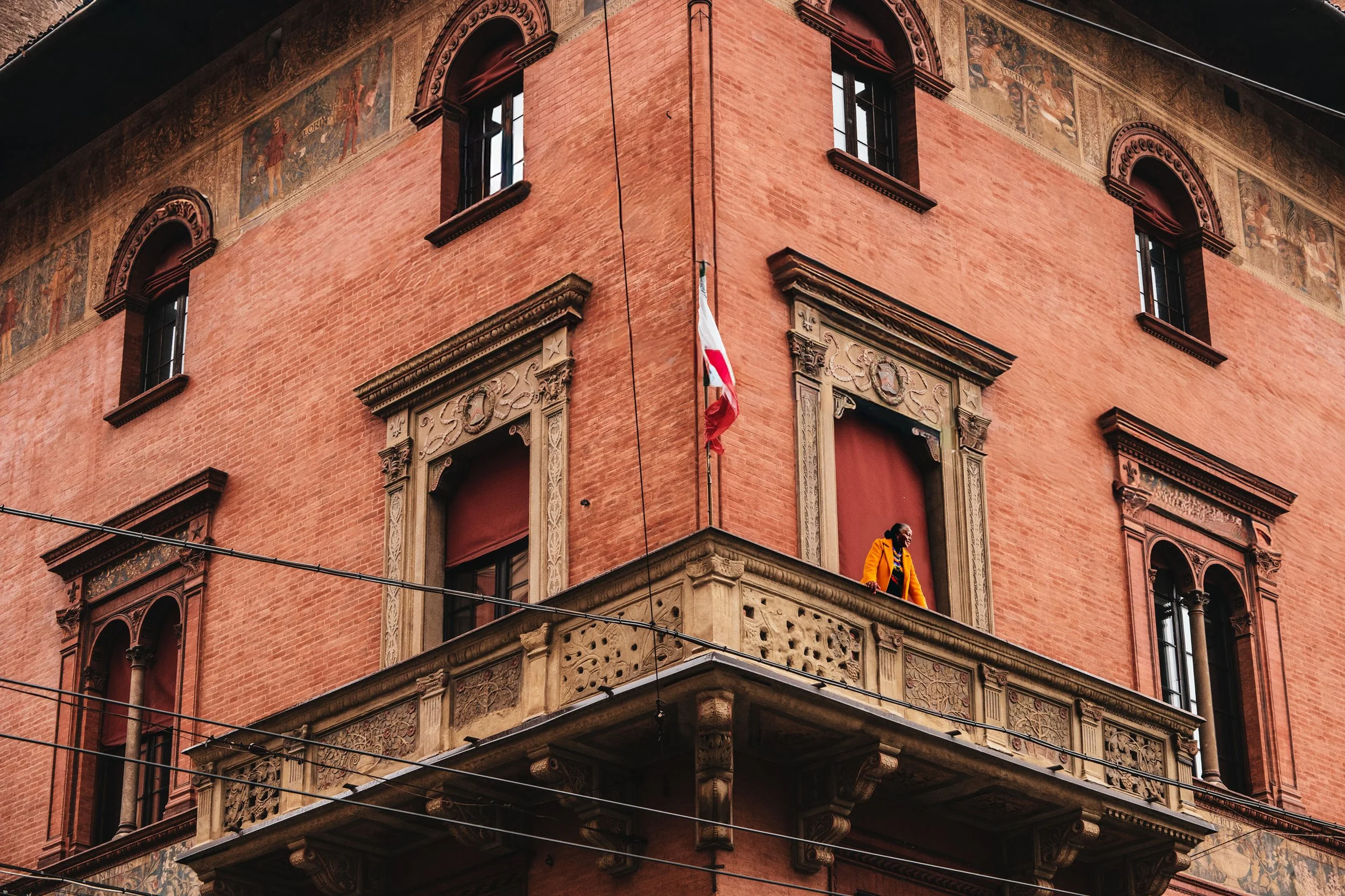 A black woman in an orange coat standing on a balcony in Bologna, Italy