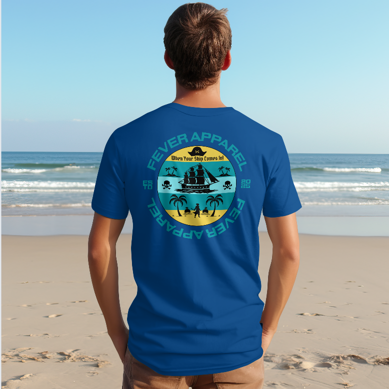 Man standing on the beach facing the ocean, wearing a blue T-shirt with a pirate ship graphic and tropical island design on the back.