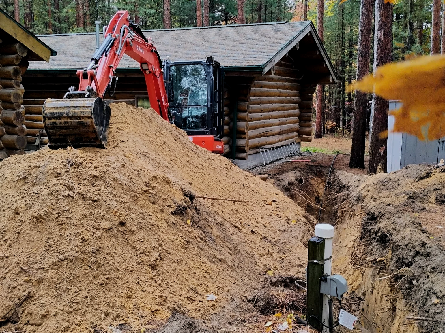 Construction site near a log cabin with an orange excavator installing septic system line
