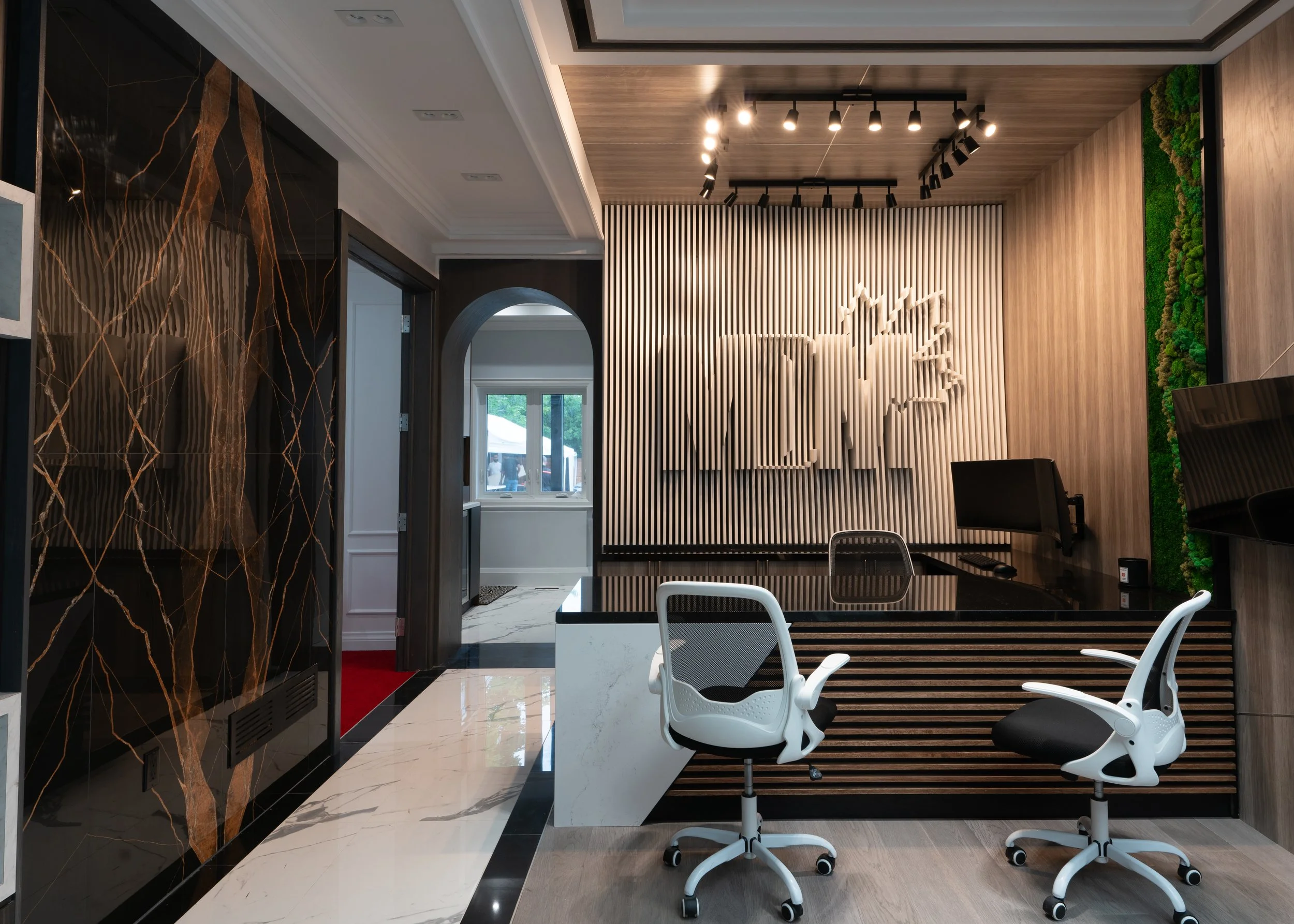 Modern office reception area with seating, a sleek desk, wall decor with vertical slats and a logo, and indoor greenery.