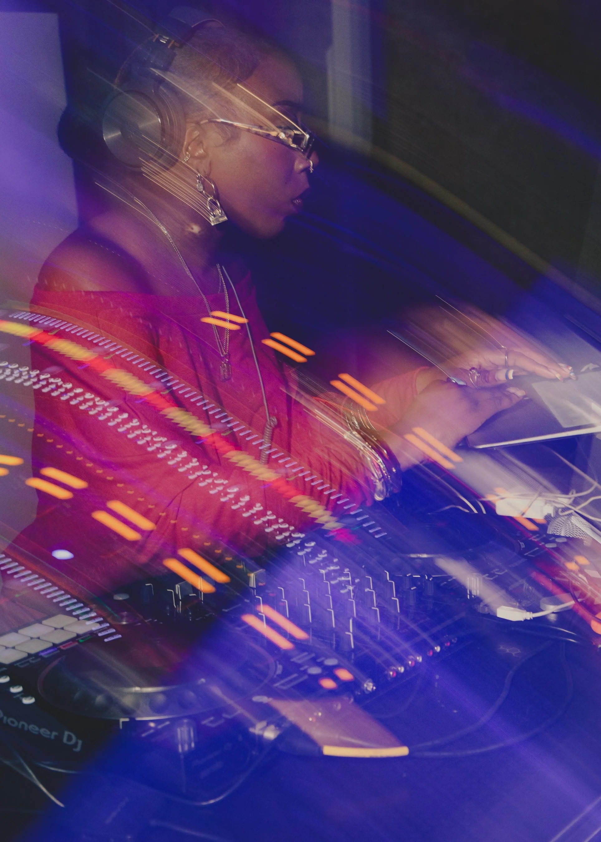 A female DJ wearing headphones and glasses, focused on mixing music on a Pioneer DJ controller, with vibrant quick motion lighting effects in the image