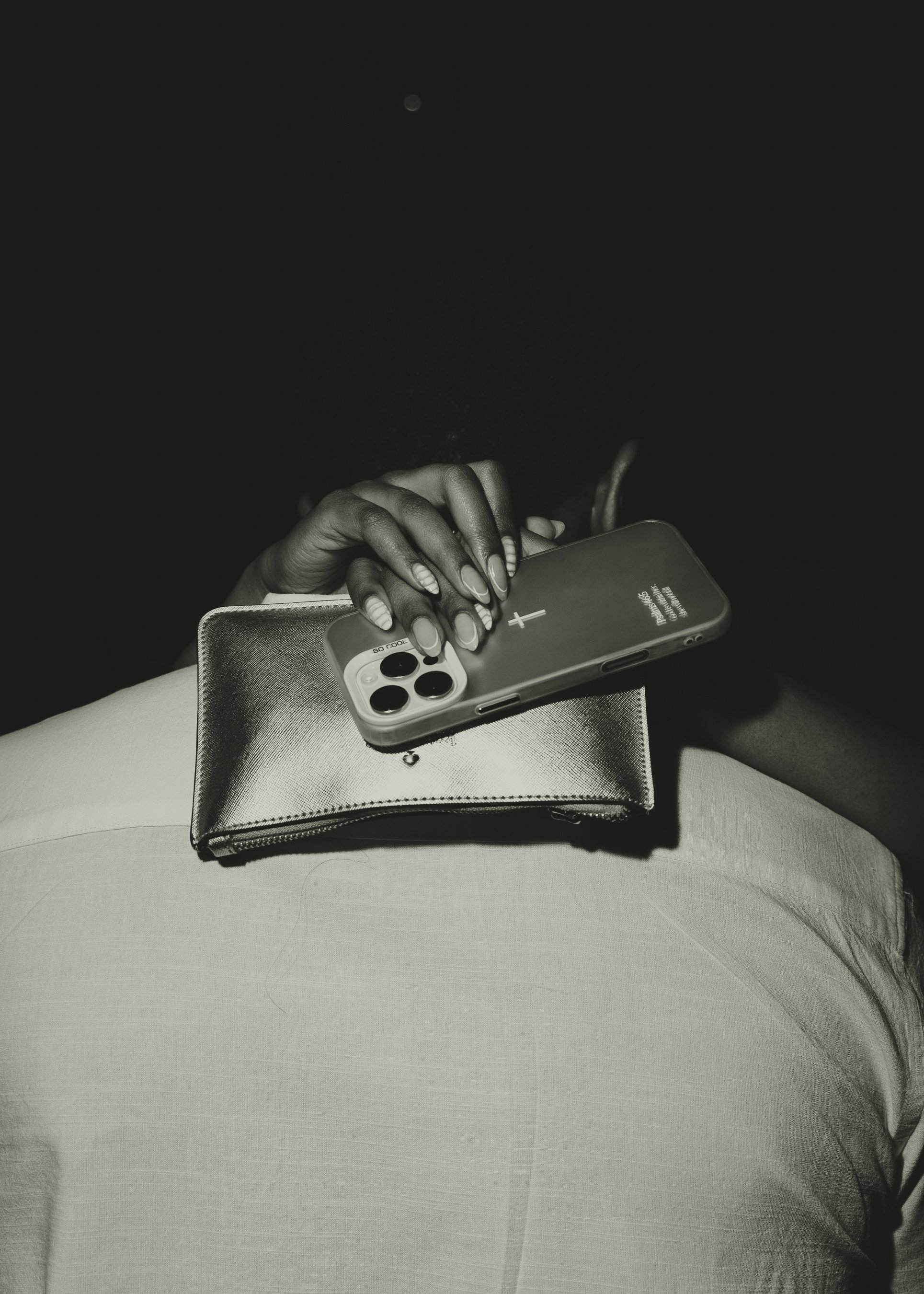 Close-up of a person's hand using a smartphone, resting on a table with a small wallet nearby, in a black-and-white photo.