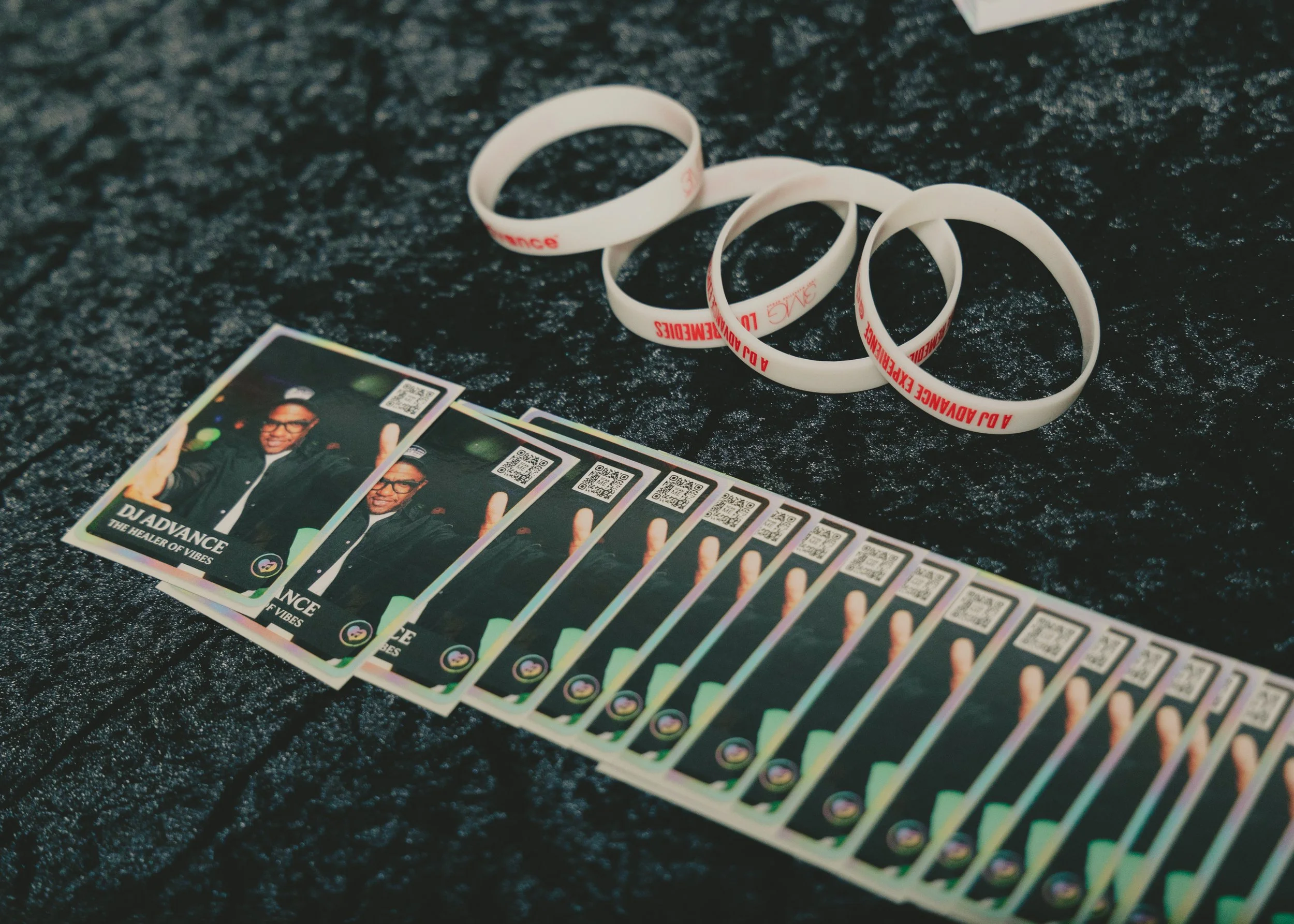 Several plastic wristbands and a stack of digital photo strips with QR codes on a black textured surface.