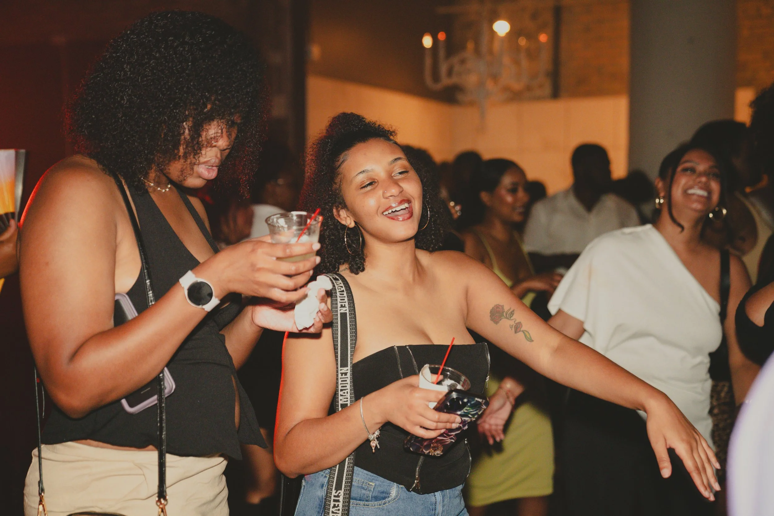 A group of women at a social event, smiling and holding drinks, in an indoor setting.