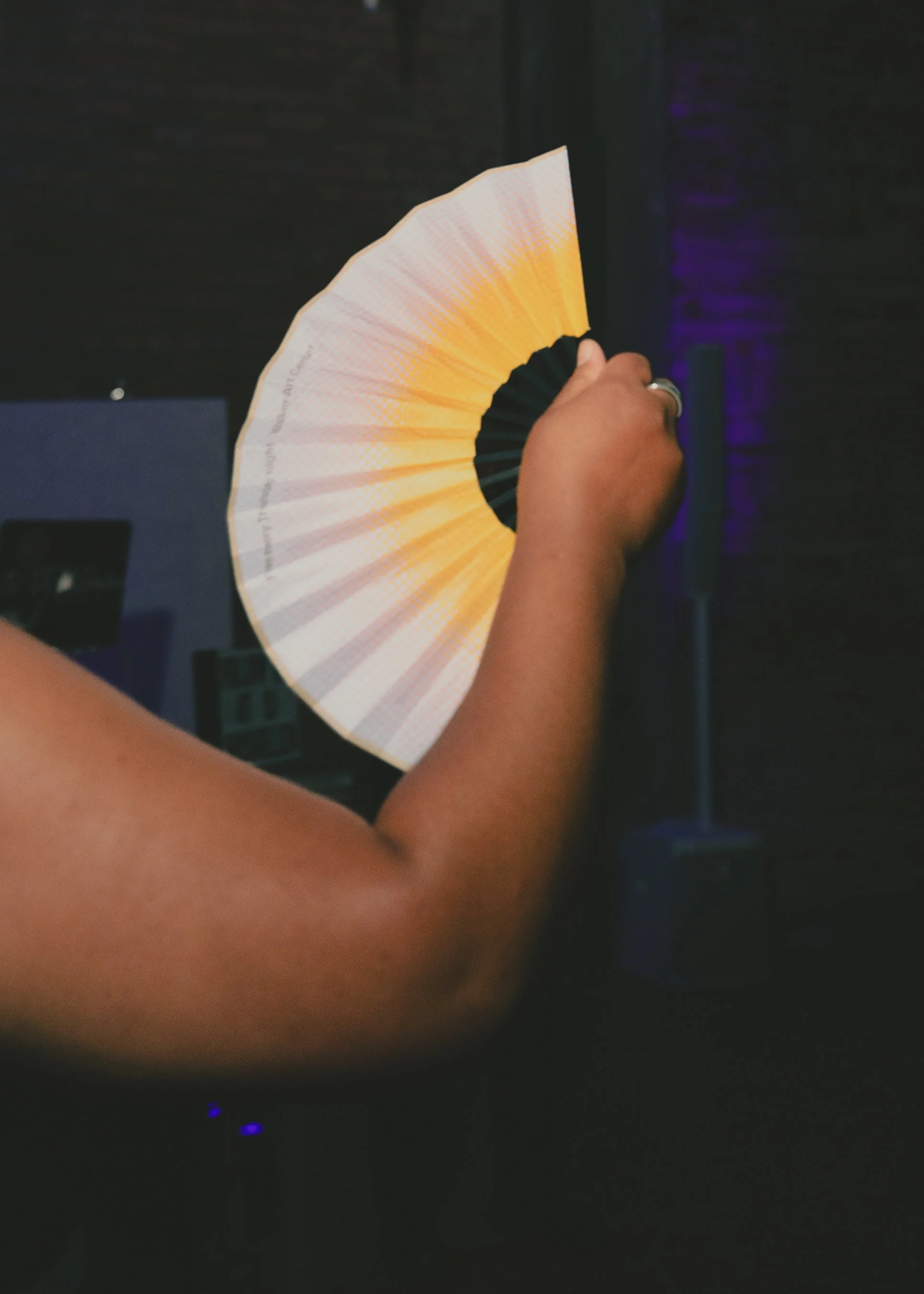 Person holding a multicolored folded paper fan with dark background.
