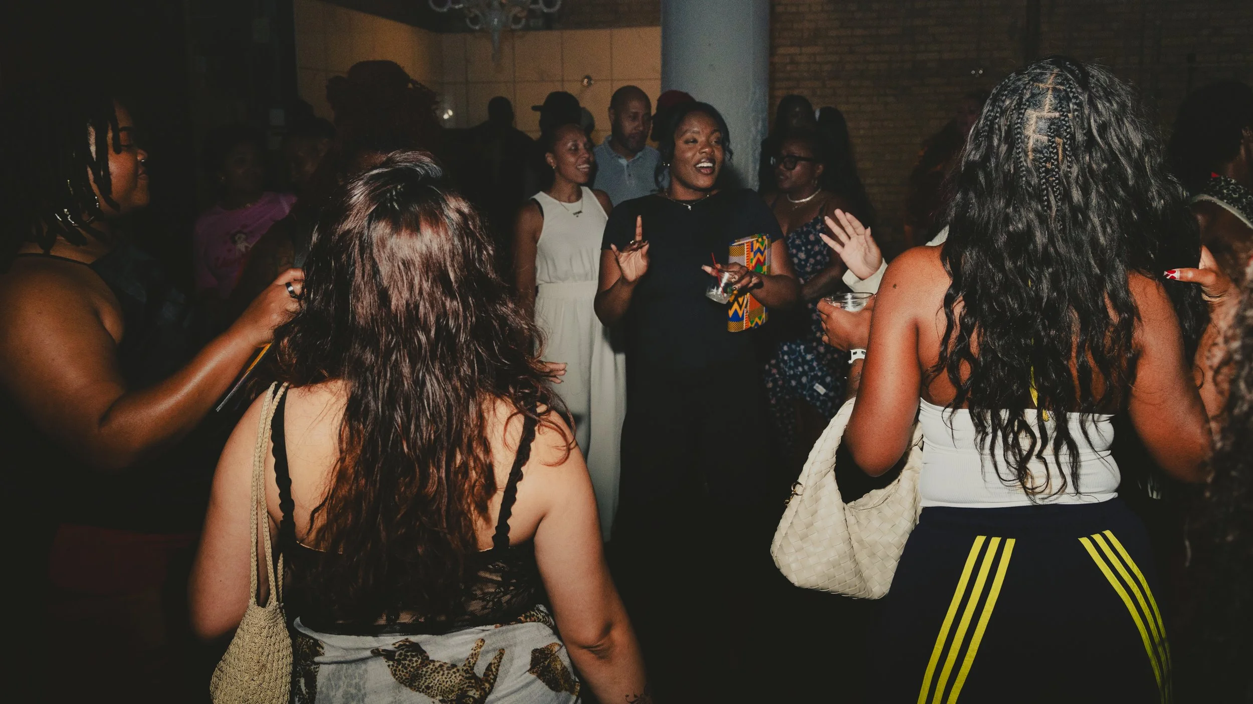 Group of people dancing and socializing at a party or event, with some holding drinks and talking.