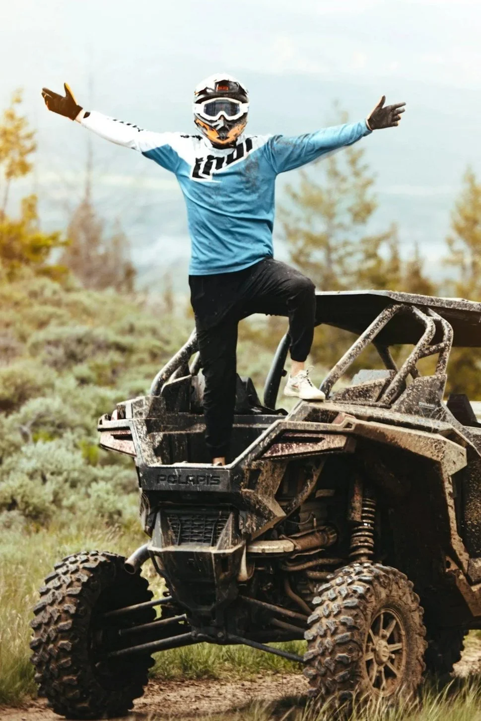 Off-road rider standing on a Polaris UTV showcasing the adventure lifestyle behind custom UTV wraps and graphics.