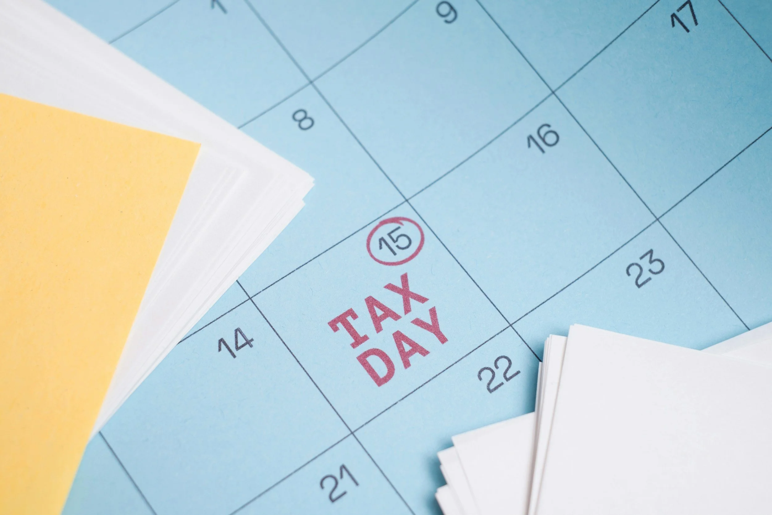 Close-up of a calendar page with a red circle around the 15th date, and the words 'TAX DAY' in red text on a blue background.